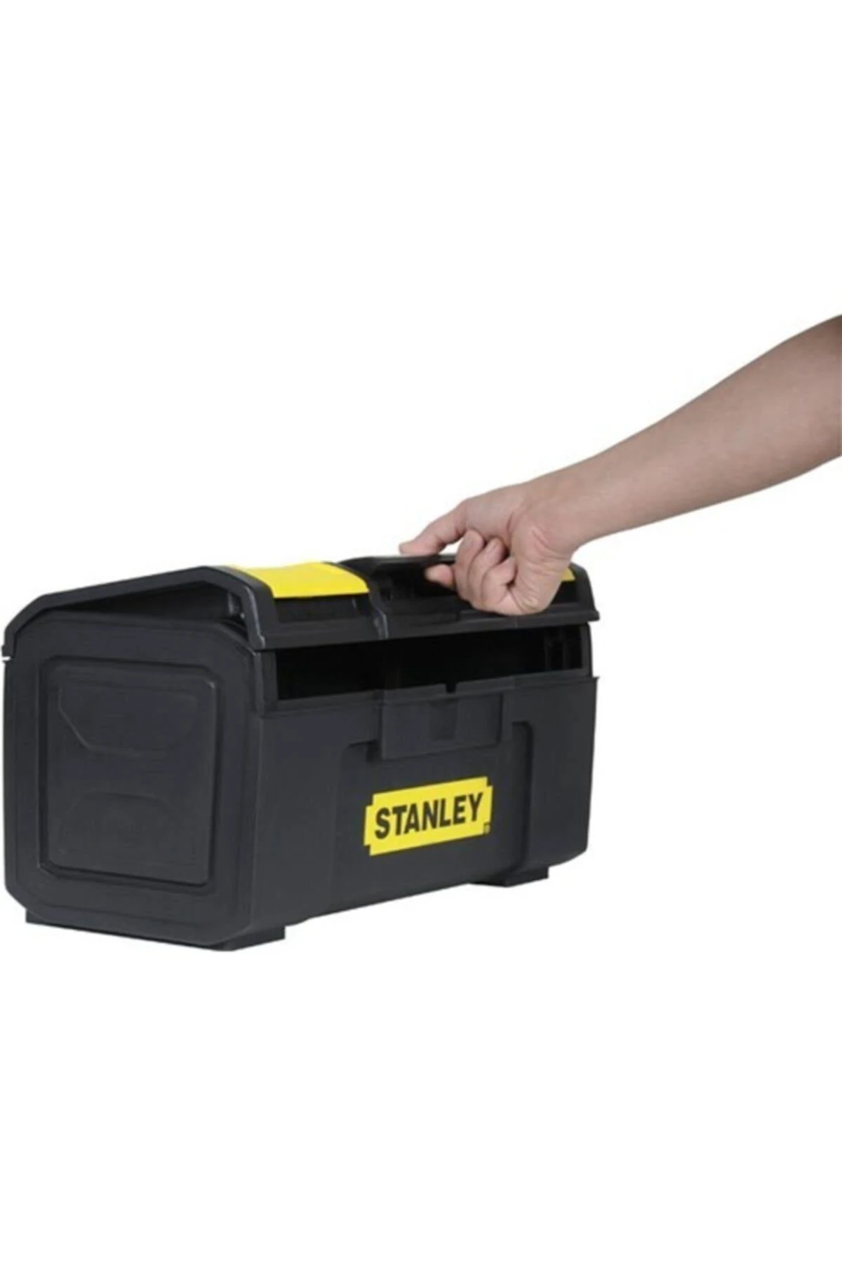 La mano de una persona sostiene una caja de herramientas Stanley negra y amarilla con el asa hacia arriba, sobre fondo blanco.