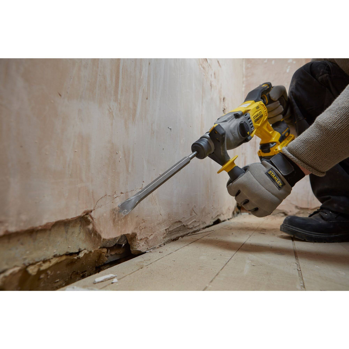 Persona usando un martillo perforador Stanley amarillo para quitar yeso de una pared.