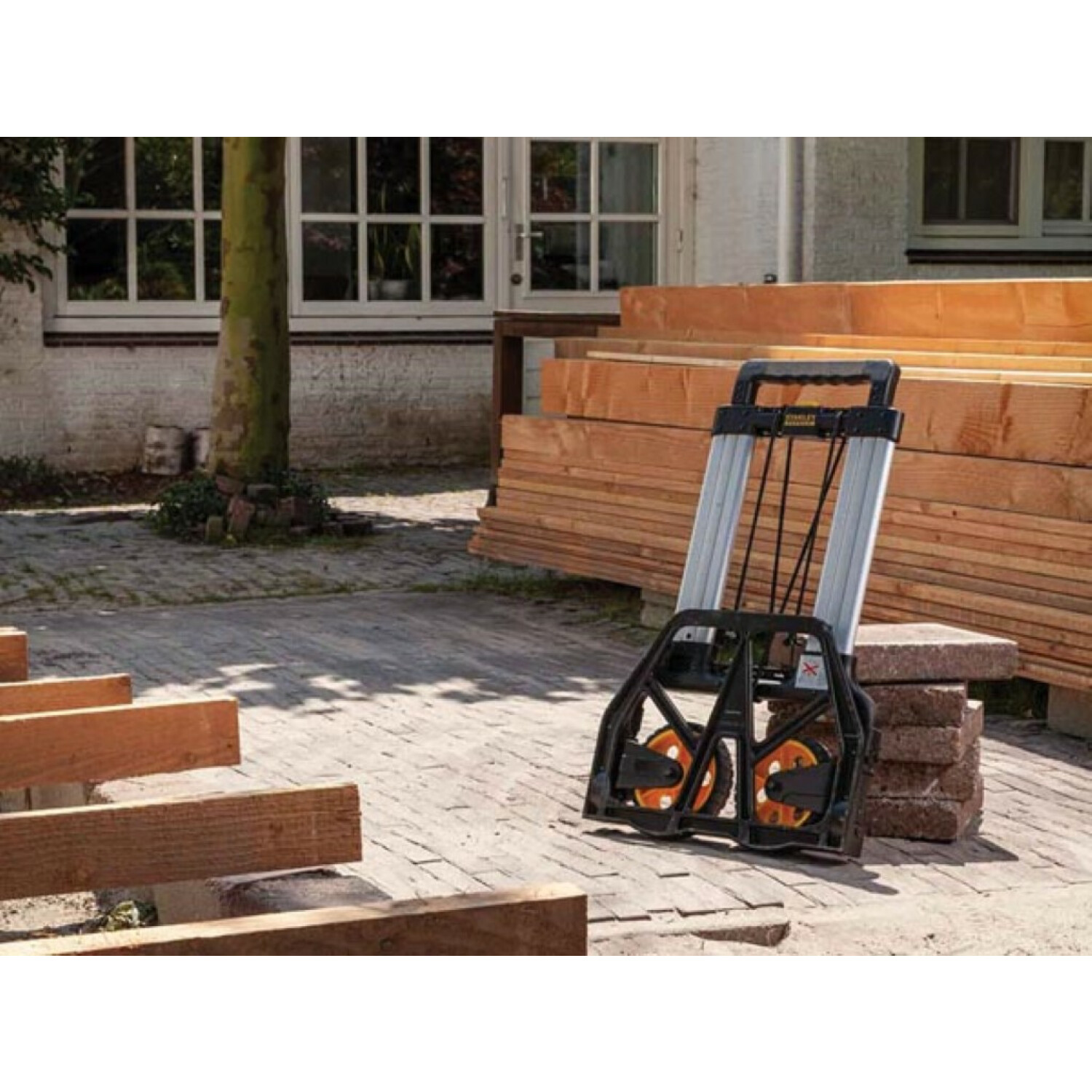 Hand truck with wood planks and brick structures, outdoors.