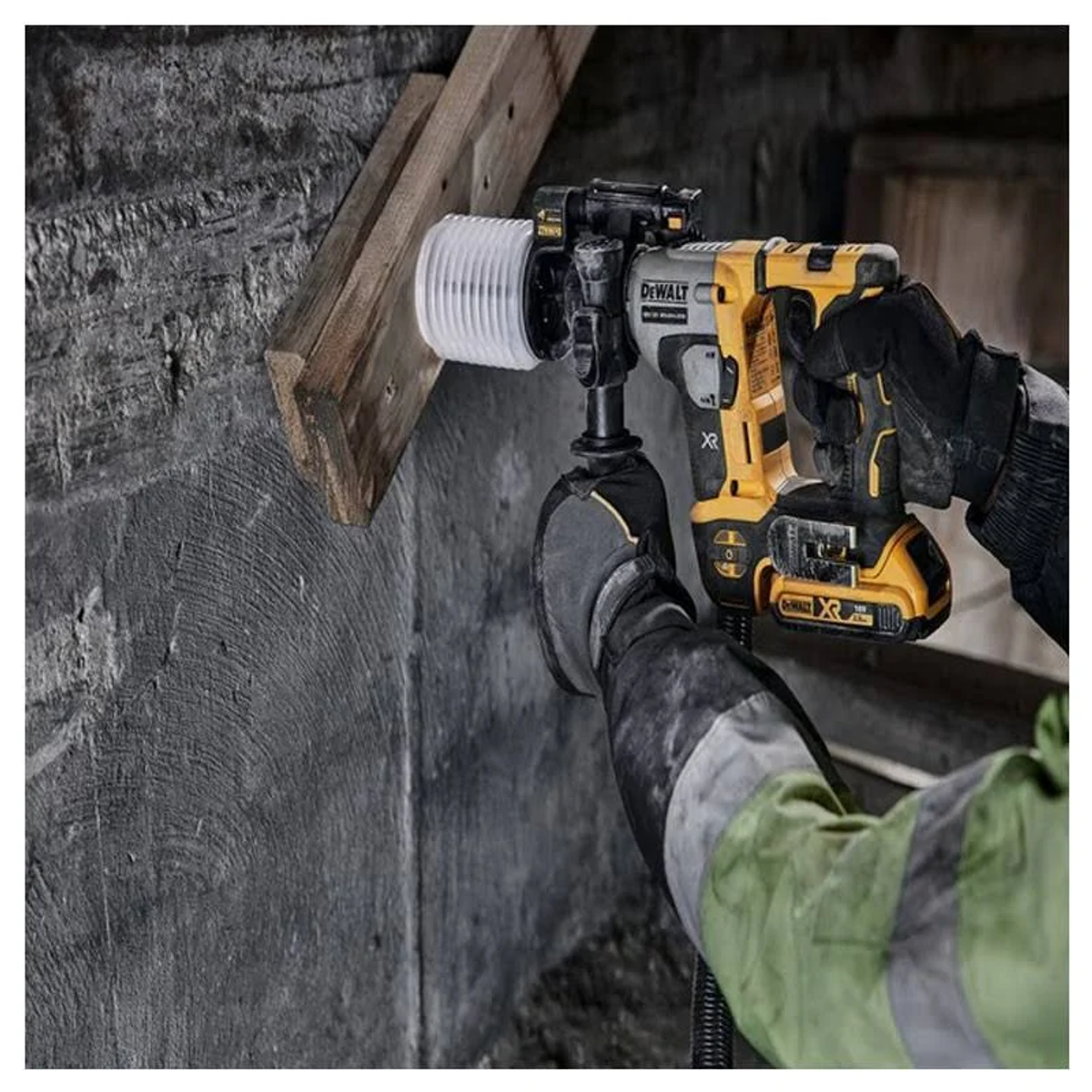 Osoba obsługująca żółto-czarną wiertarkę Dewalt na szarej ścianie.