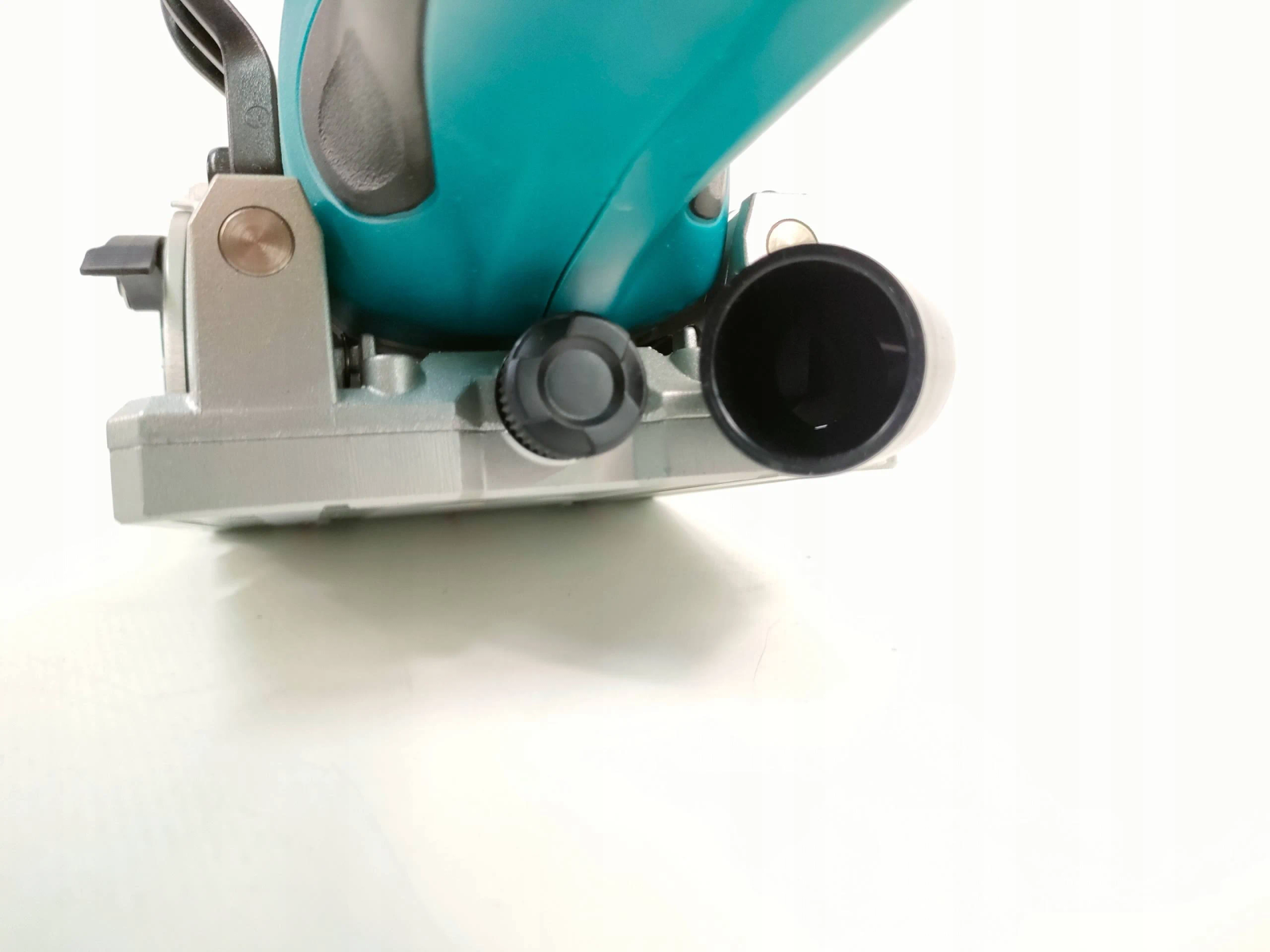 Narzędzie elektryczne w kolorze turkusowym i srebrnym, prawdopodobnie piła tarczowa, na białym tle.