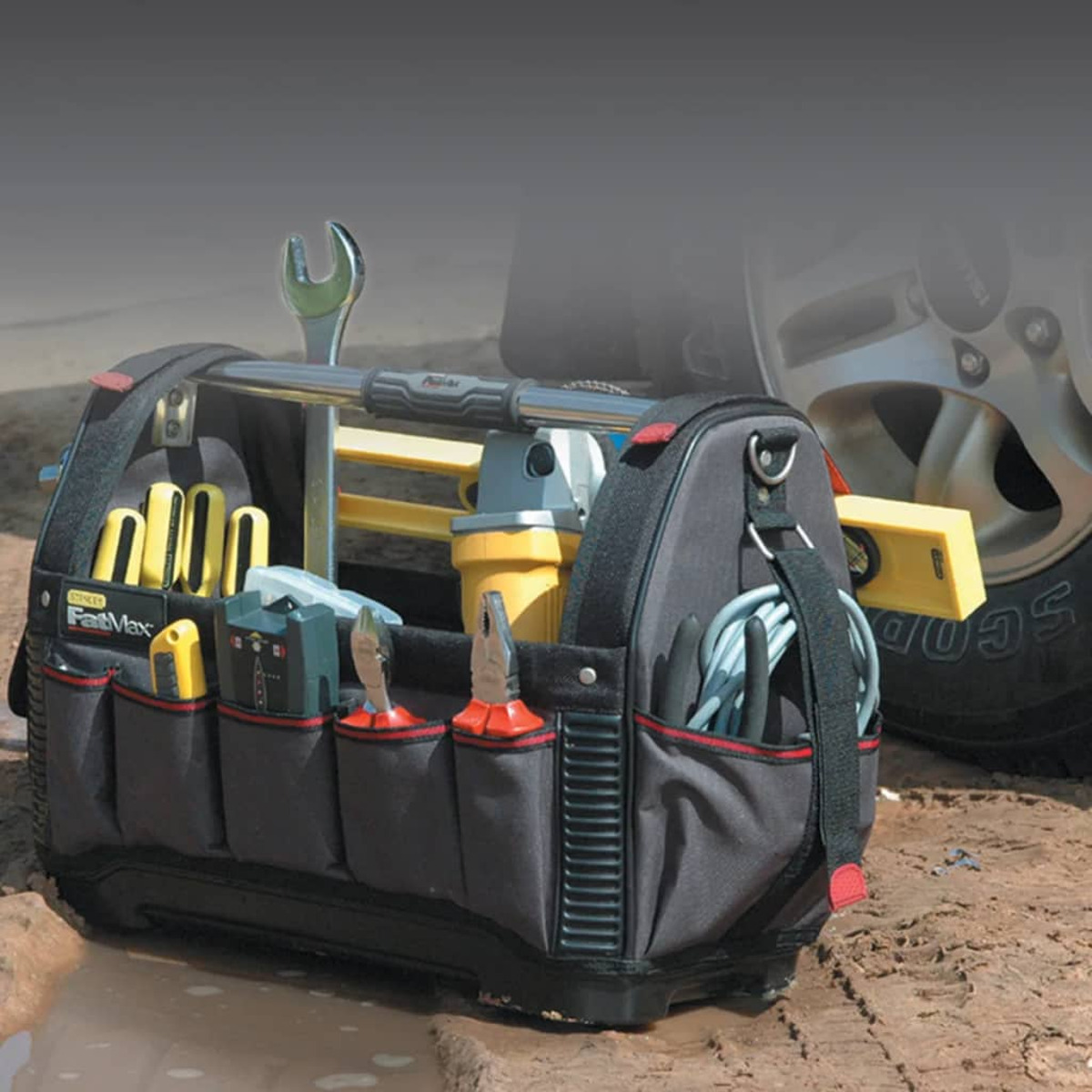 Una borsa nera con attrezzi all'interno. La borsa è su un terreno sporco con uno pneumatico per auto sullo sfondo.