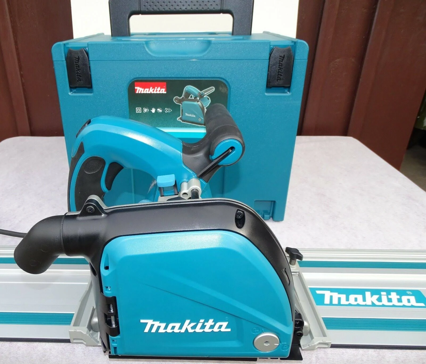 Una sega circolare Makita turchese e nera con una custodia turchese su una superficie bianca.