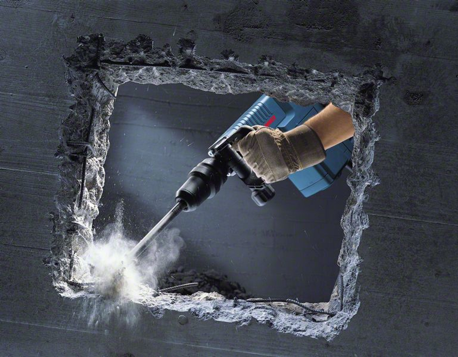 Una persona che usa un martello pneumatico blu e nero sta sfondando un muro di cemento. Polvere che vola.