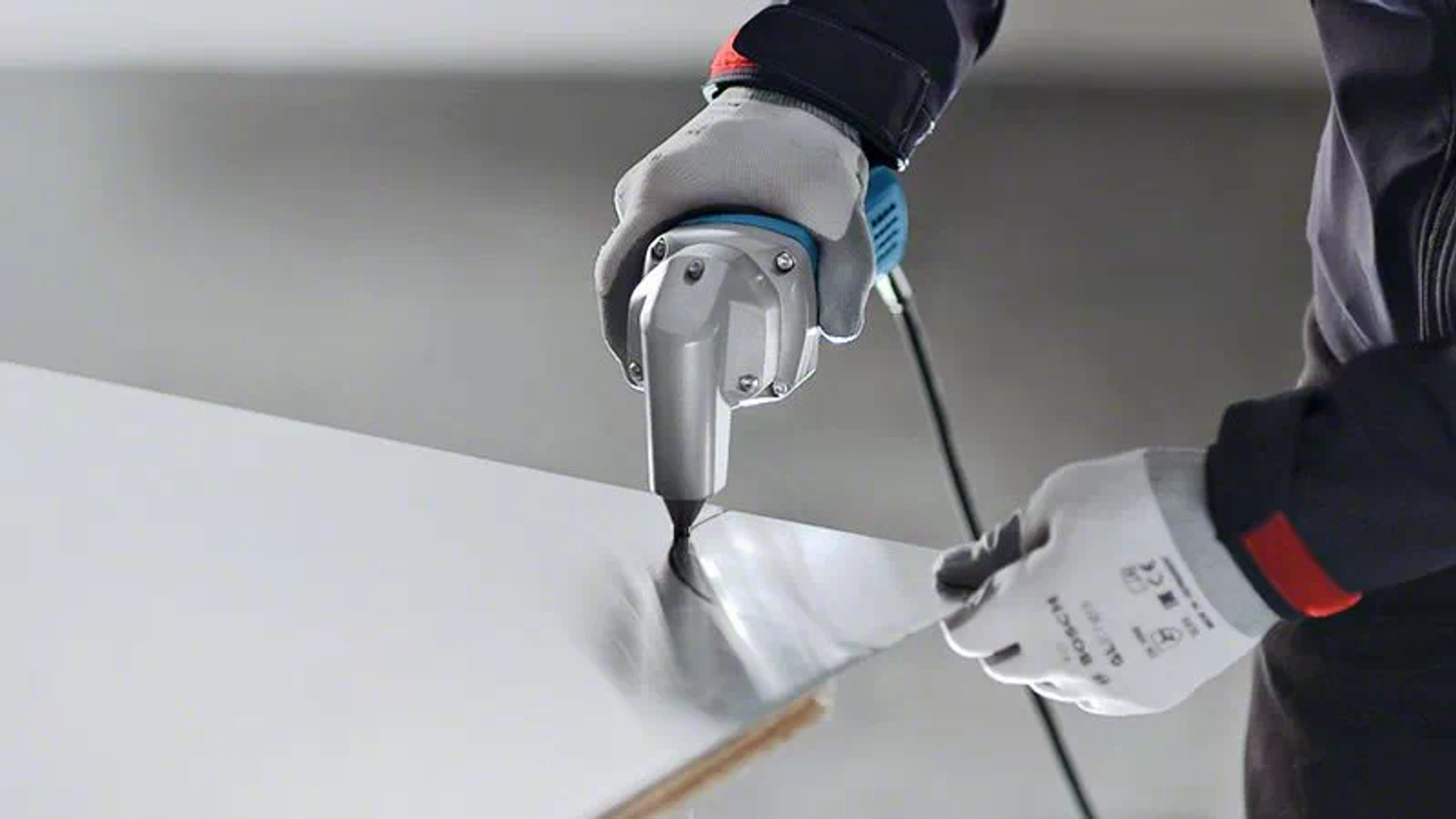 Un operaio usa una cesoia elettrica argentata per tagliare un foglio bianco, indossando guanti.