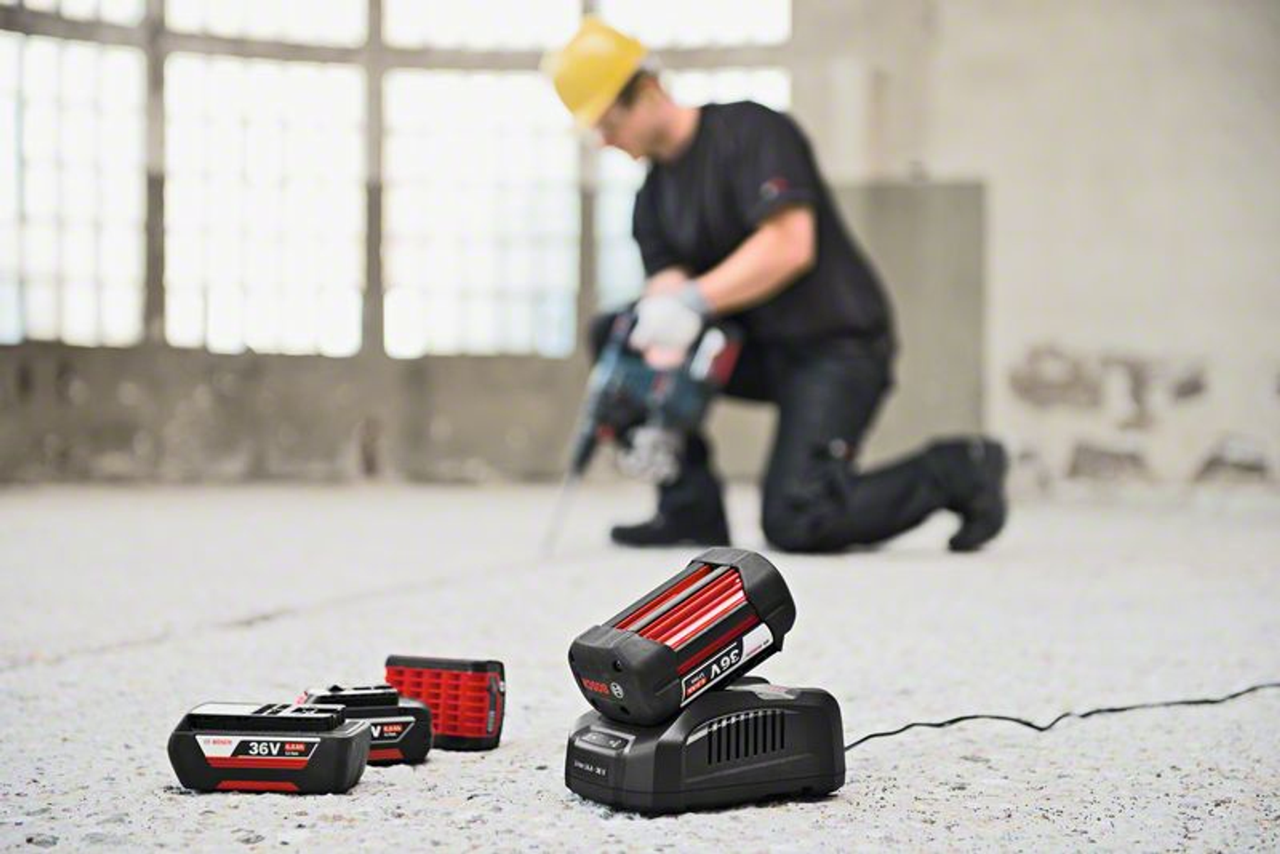Bosch piller ve şarj cihazı, arka planda matkap kullanan bir adamla.