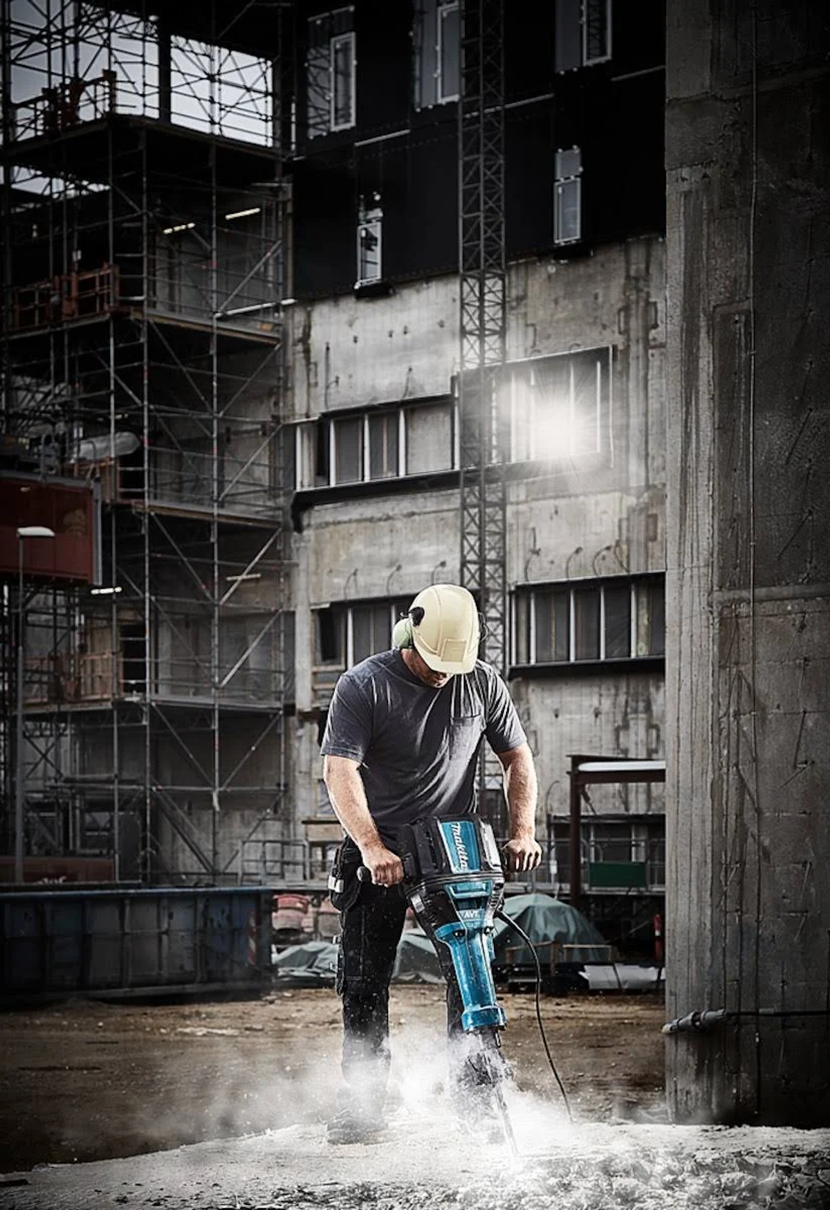 Uomo che usa un martello demolitore Makita sul cemento. Sfondo cantiere.