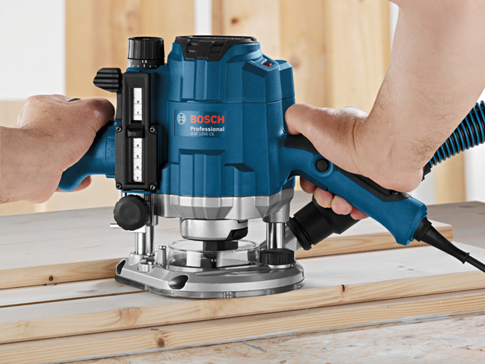 Mani che azionano una fresatrice Bosch blu sul legno. L'utensile è su una superficie di legno.