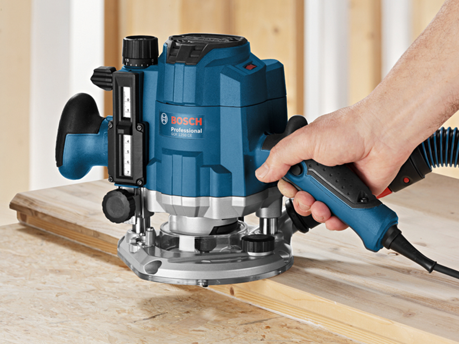 Fresatrice Bosch blu su legno. Mano della persona che tiene in mano l'utensile. Venatura del legno visibile.
