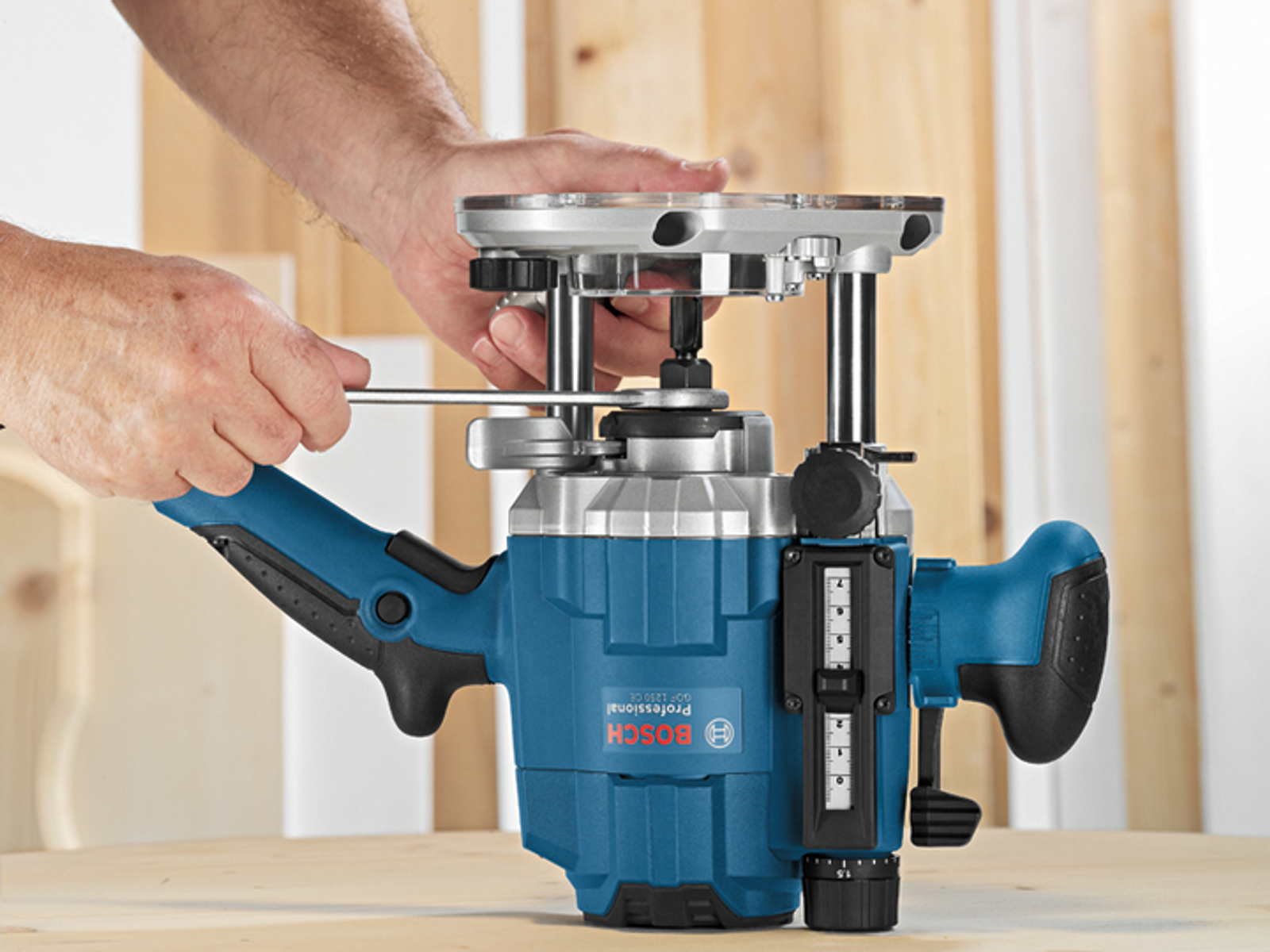Router Bosch blu e argento su cui sta lavorando una persona con una chiave inglese. Il router è su un tavolo di legno.