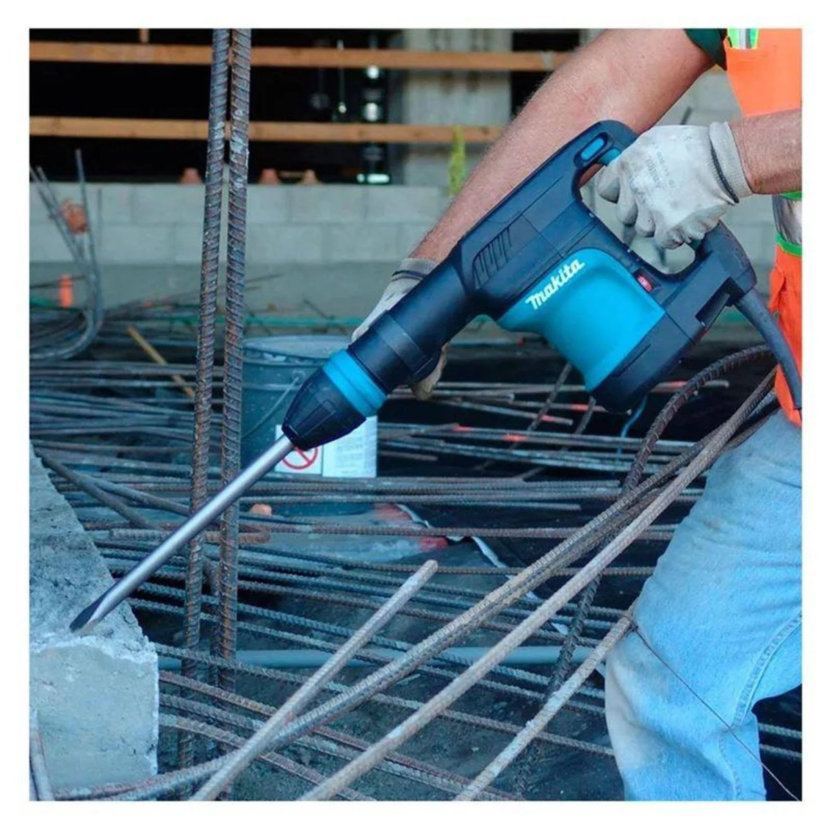 Un trabajador usa un martillo perforador Makita teal sobre hormigón, con barras de refuerzo.