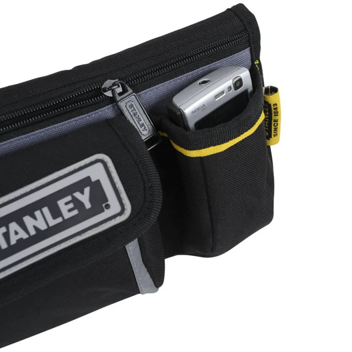 Bolsa de herramientas Stanley negra con teléfono en un bolsillo. Cremallera y etiqueta Stanley visibles.