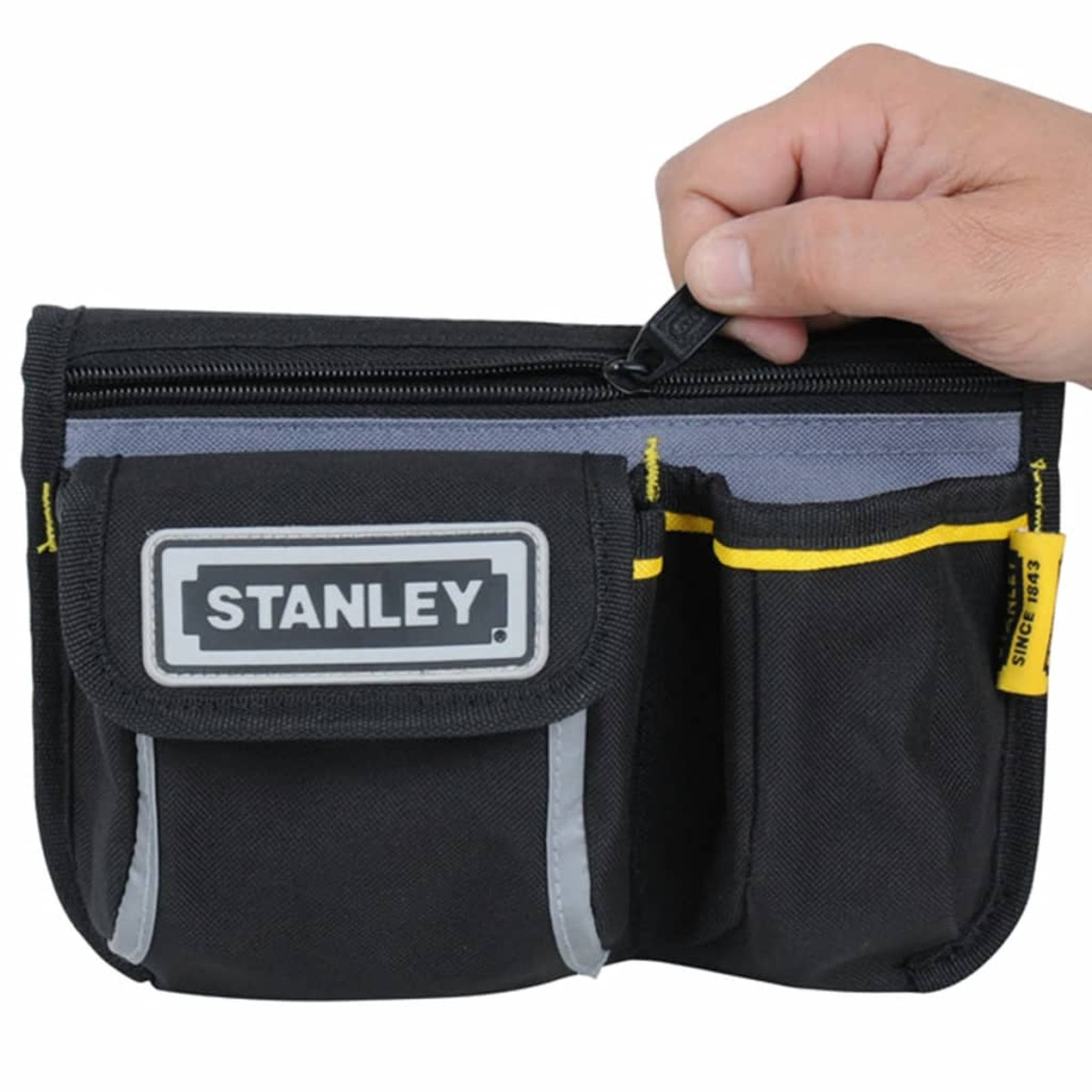 La mano de una persona desabrochando una bolsa de herramientas Stanley negra y gris. Acentos amarillos.