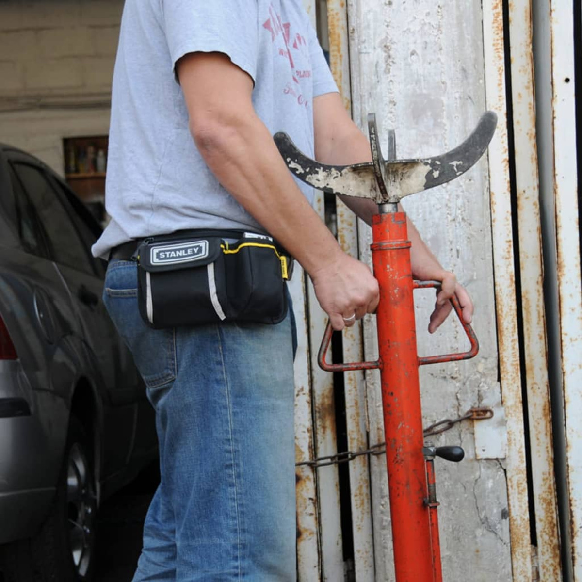 Un hombre en jeans y camisa gris sostiene un gato rojo y naranja. Una riñonera negra en la cintura.