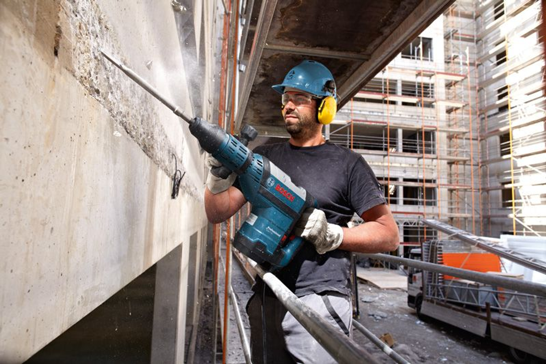 Un operaio fora il cemento con un elettroutensile. Sullo sfondo, un edificio in costruzione.