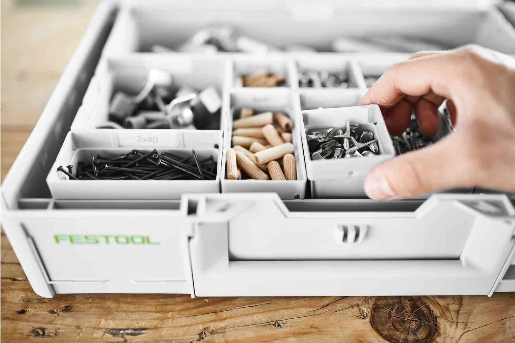 Una mano che seleziona oggetti da un organizer di utensili Festool con vari scomparti.
