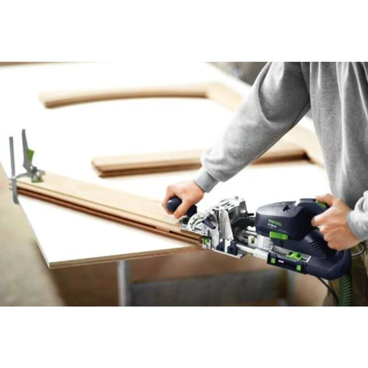 Una persona usa un utensile per la lavorazione del legno su una tavola di legno. La macchina è nera e verde.