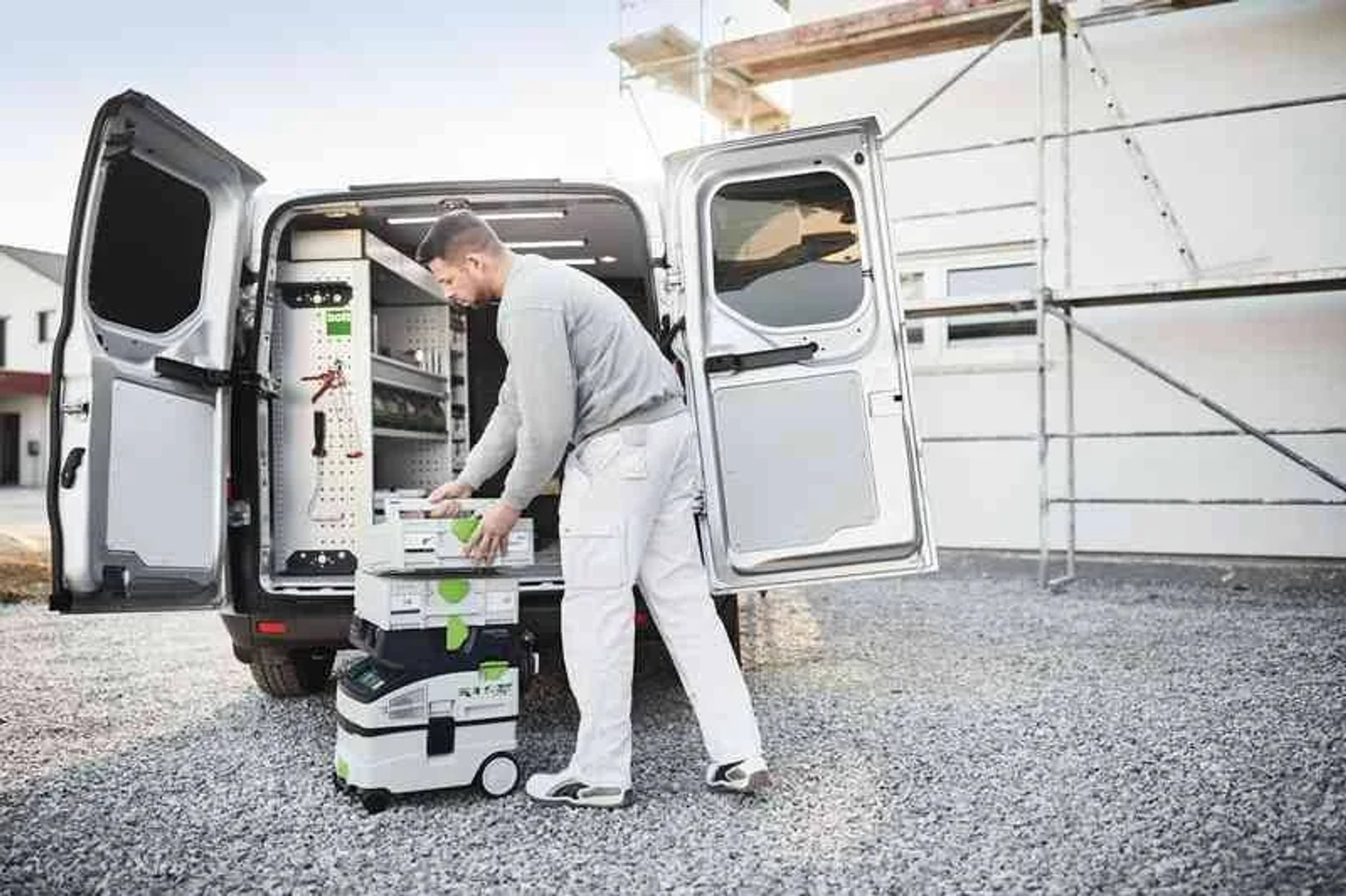 Mann lädt Festool-Aufbewahrungsboxen in einen auf Kies geparkten Transporter.