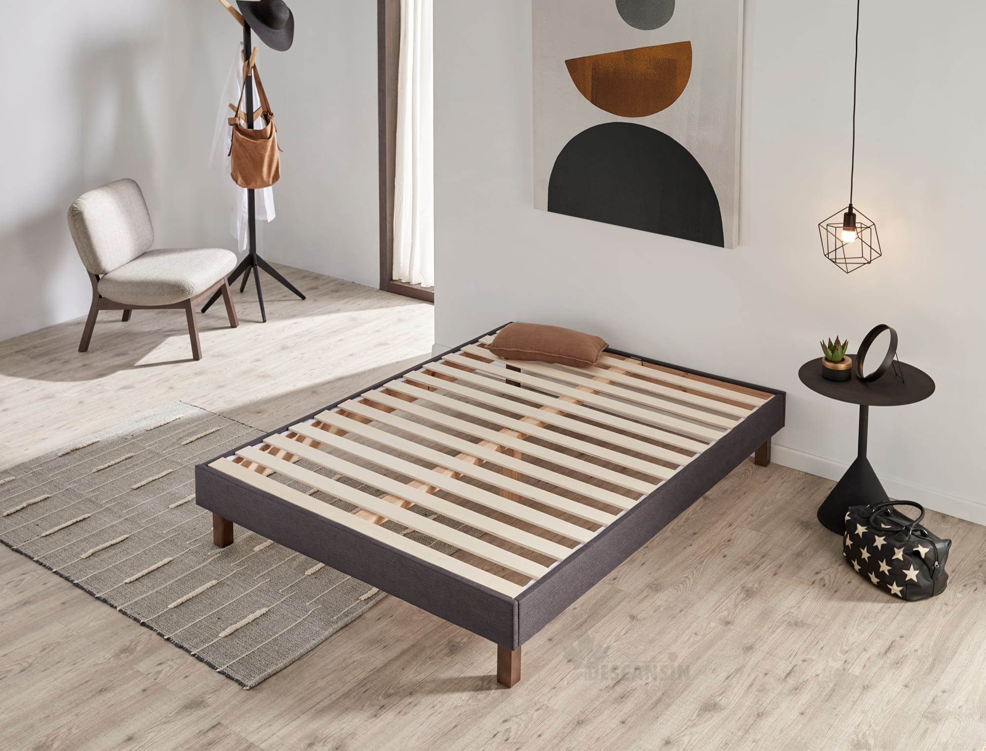 Un marco de cama gris con listones de madera en una habitación con alfombra, silla y arte.