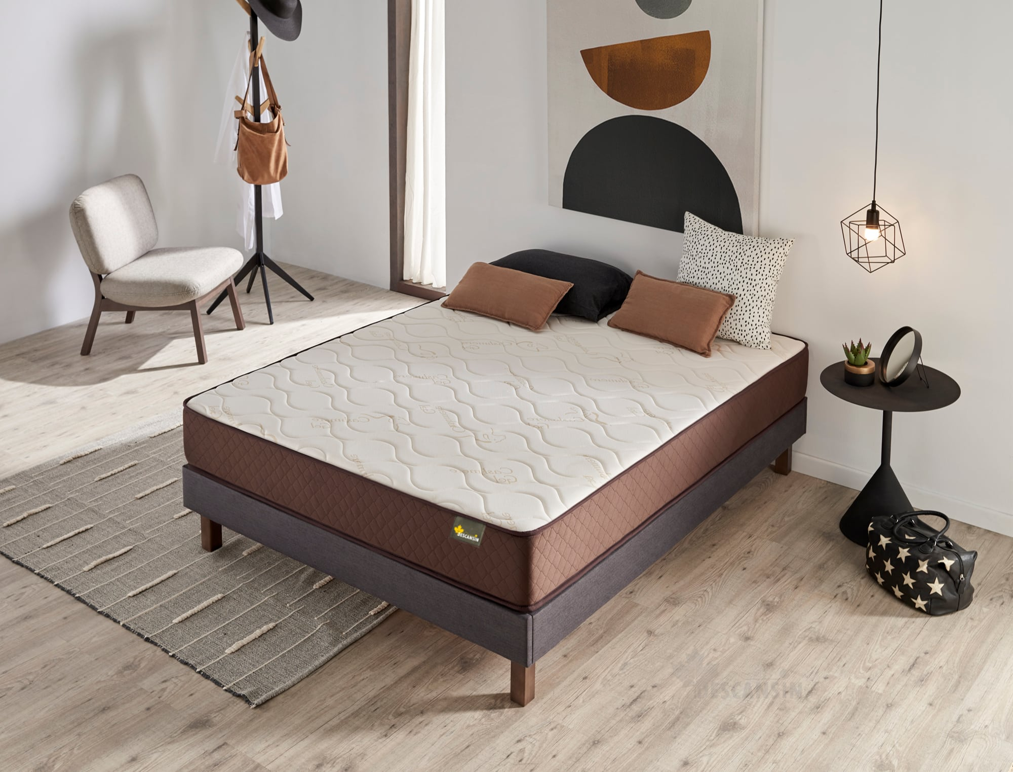 Una escena de dormitorio con una cama. La cama tiene un colchón marrón. Hay almohadas, una alfombra y una lámpara.