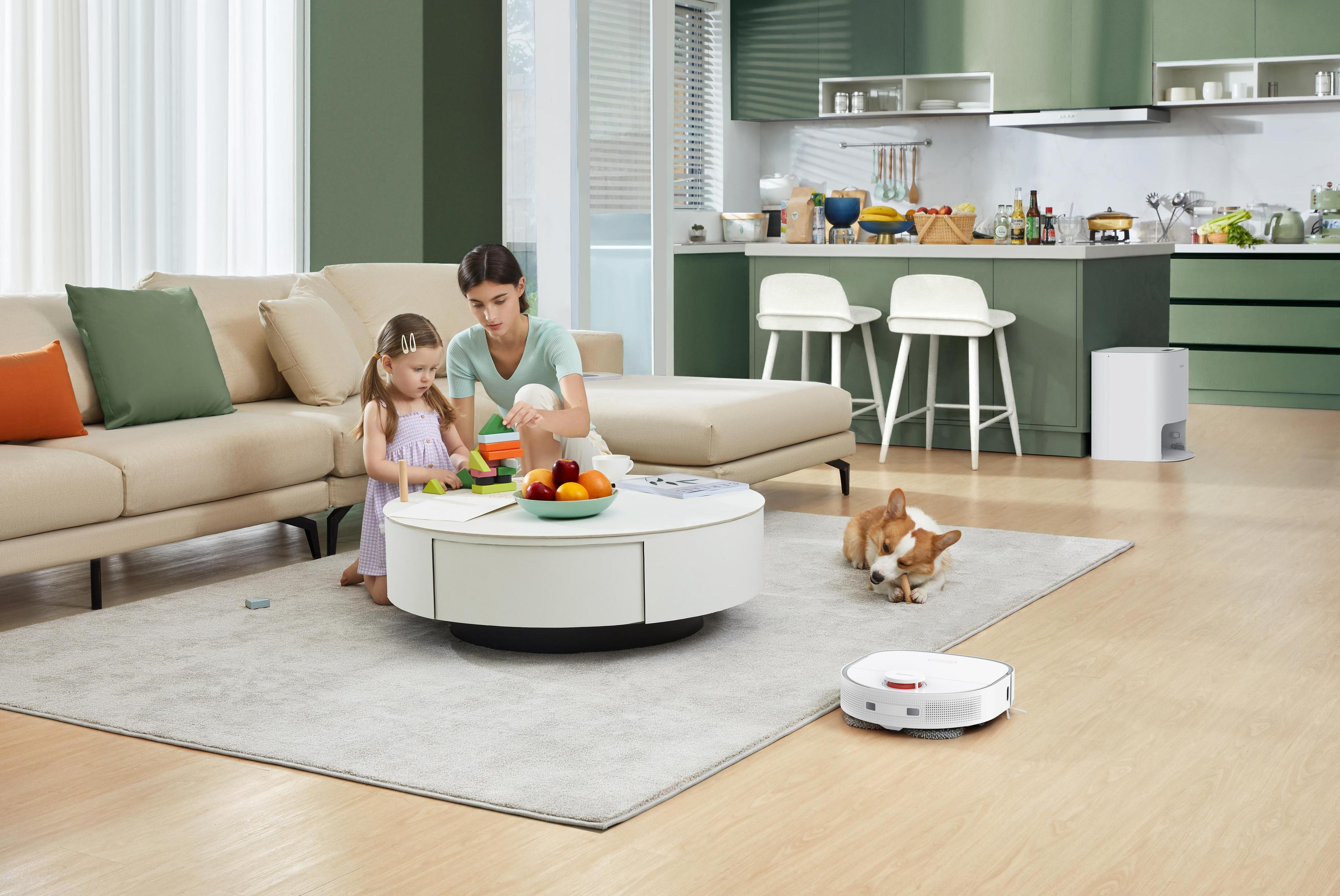 Frau und Kind spielen mit Blöcken am Tisch. Hund und Roboter-Staubsauger auf dem Boden.