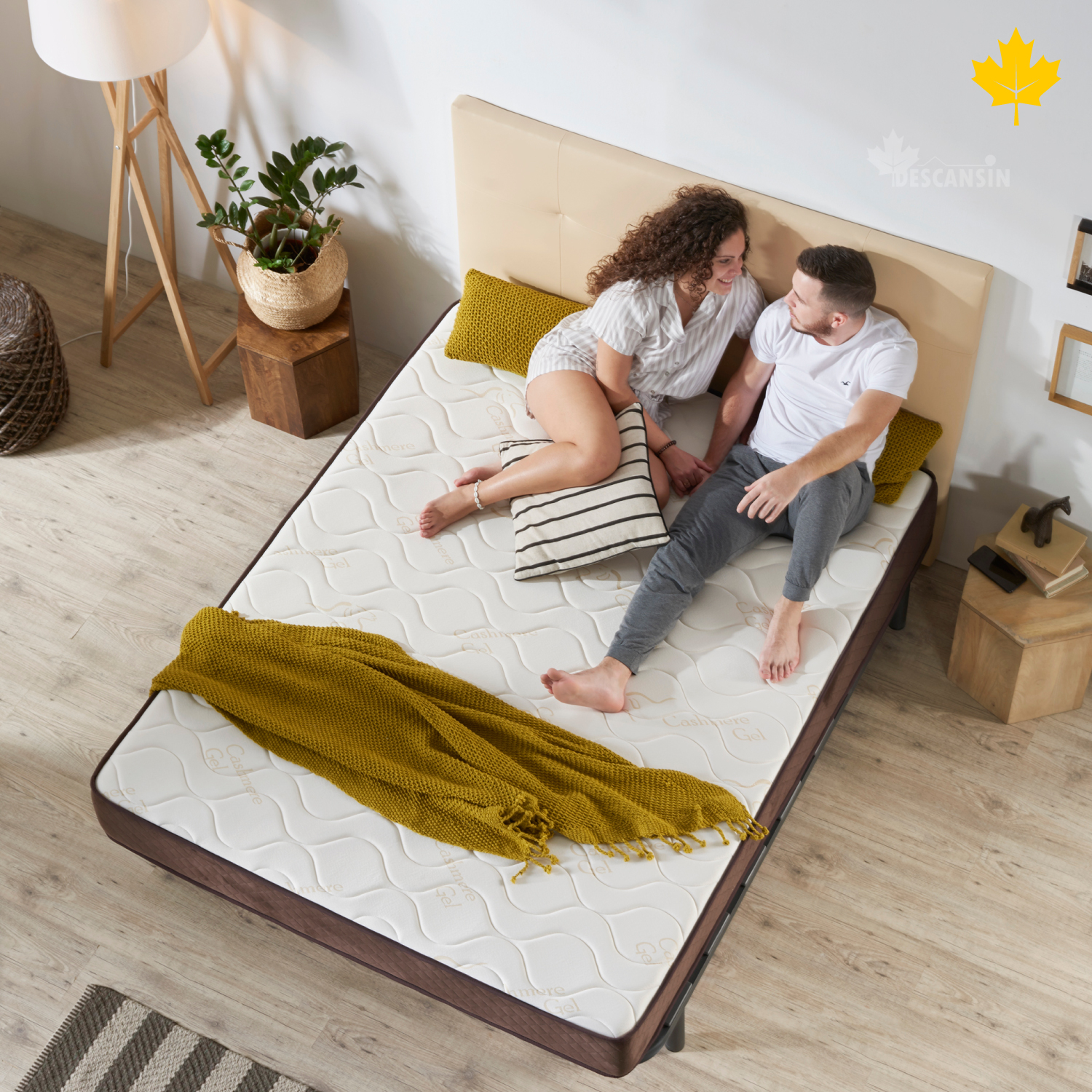 Una pareja en una cama, mirándose el uno al otro. La cama tiene un colchón marrón y una manta amarilla.