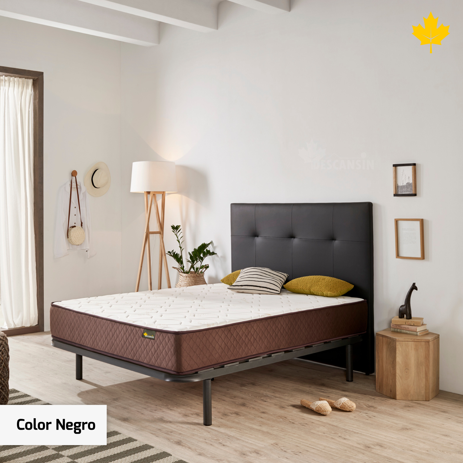 Dormitorio con marco de cama negro, colchón blanco y cabecero negro. Hay una lámpara y decoración.