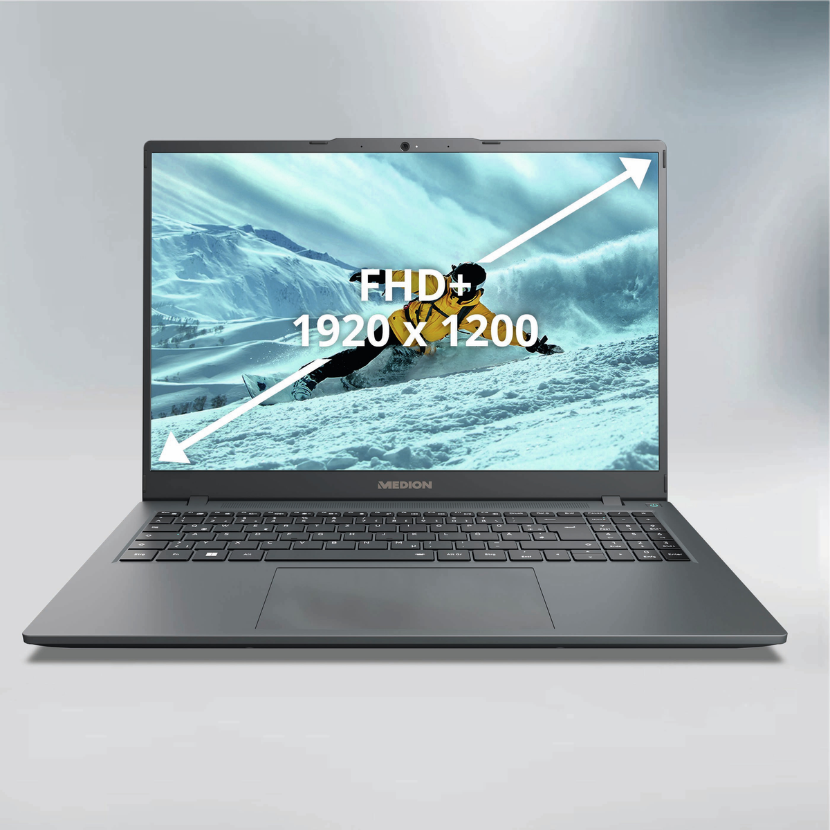 Laptop wyświetla narciarza na zaśnieżonej górze. Tekst na ekranie: FHD+, 1920 x 1200. Laptop jest szary, z logo Medion.