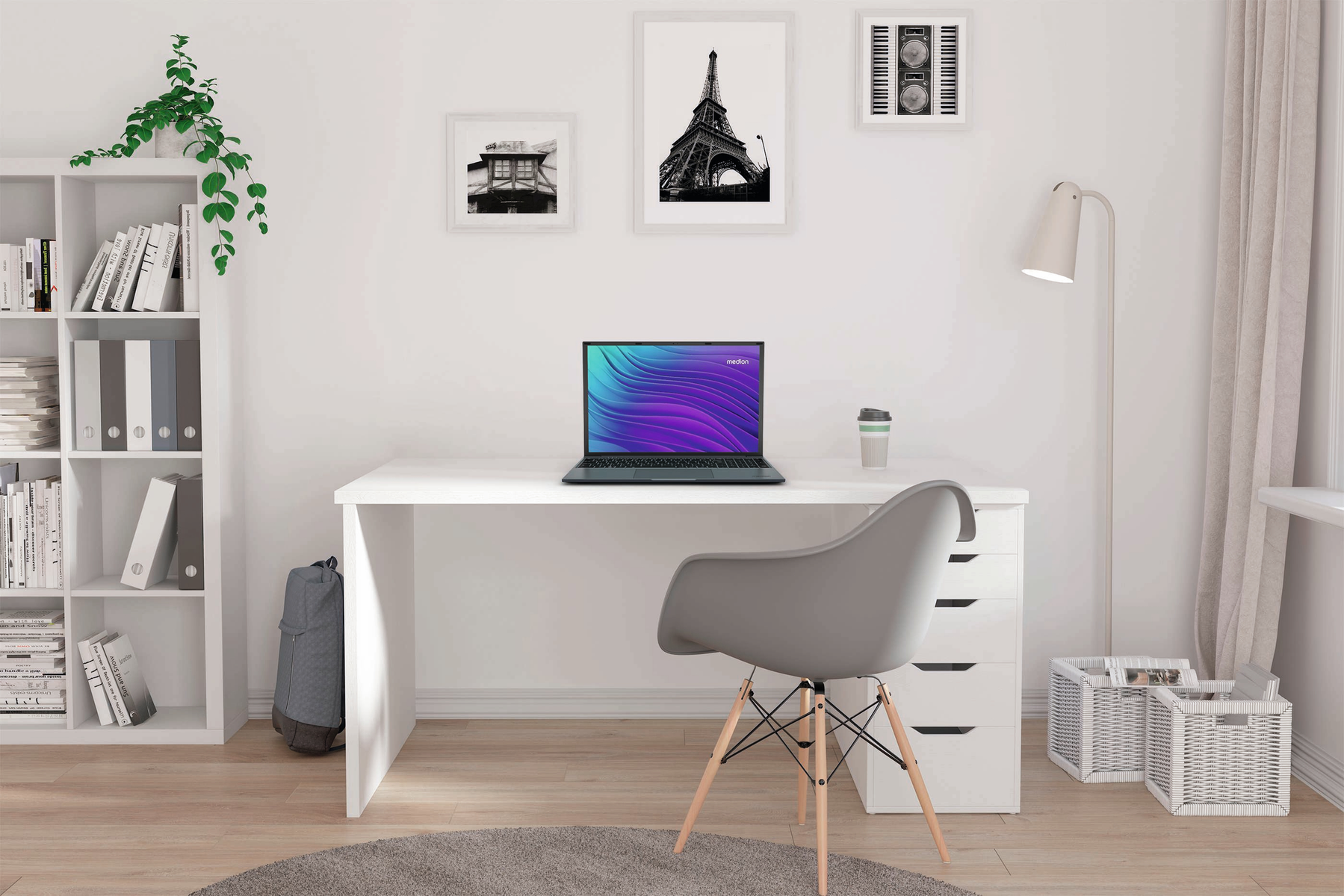 Domowe biuro z białym biurkiem, laptopem i szarym krzesłem. Wiszą obrazy. Jest regał i plecak. Widoczna jest roślina.