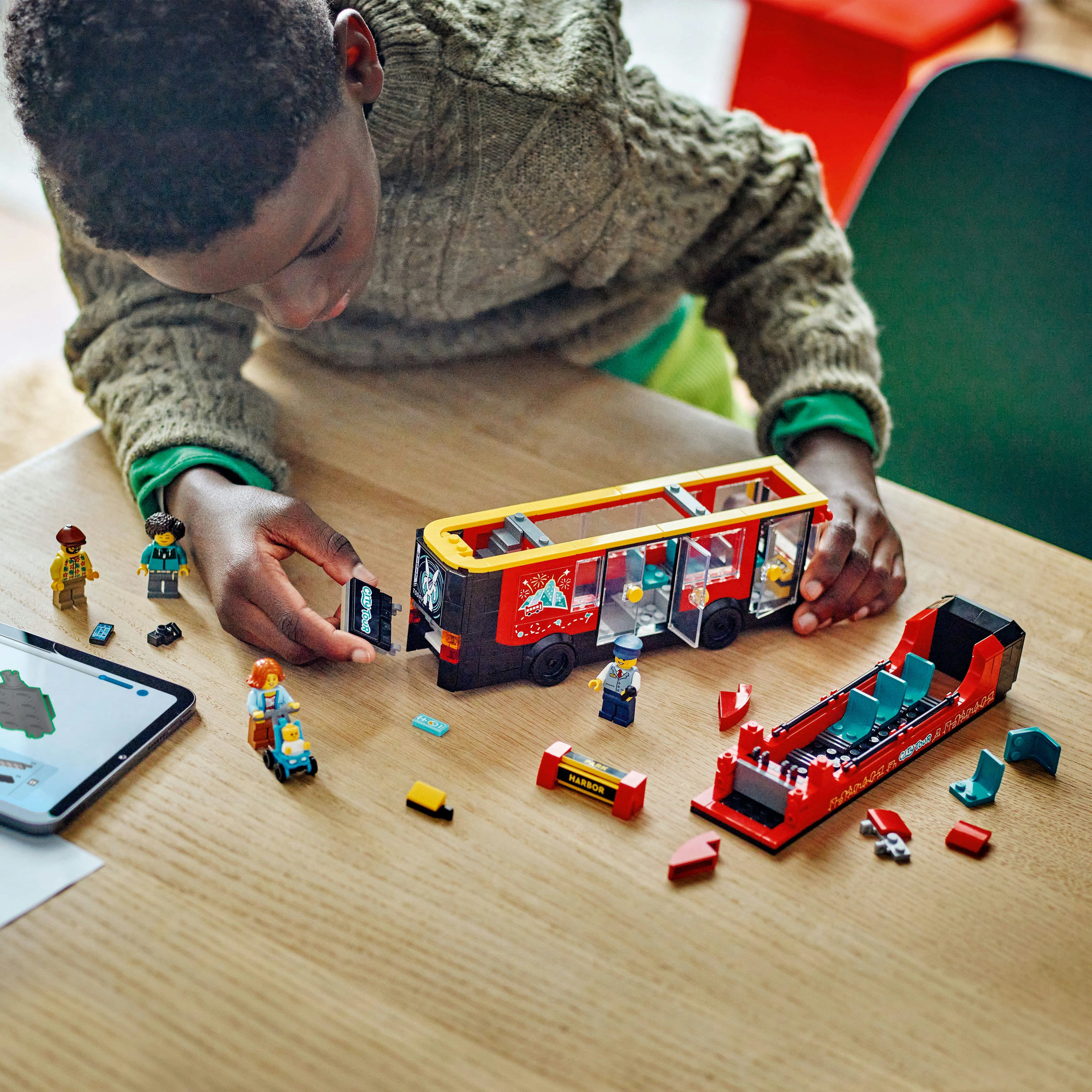 Bir çocuk Lego otobüs oyuncağı yapıyor. Otobüs, mini figürler ve parçalarla kırmızı, sarı ve siyahtır.