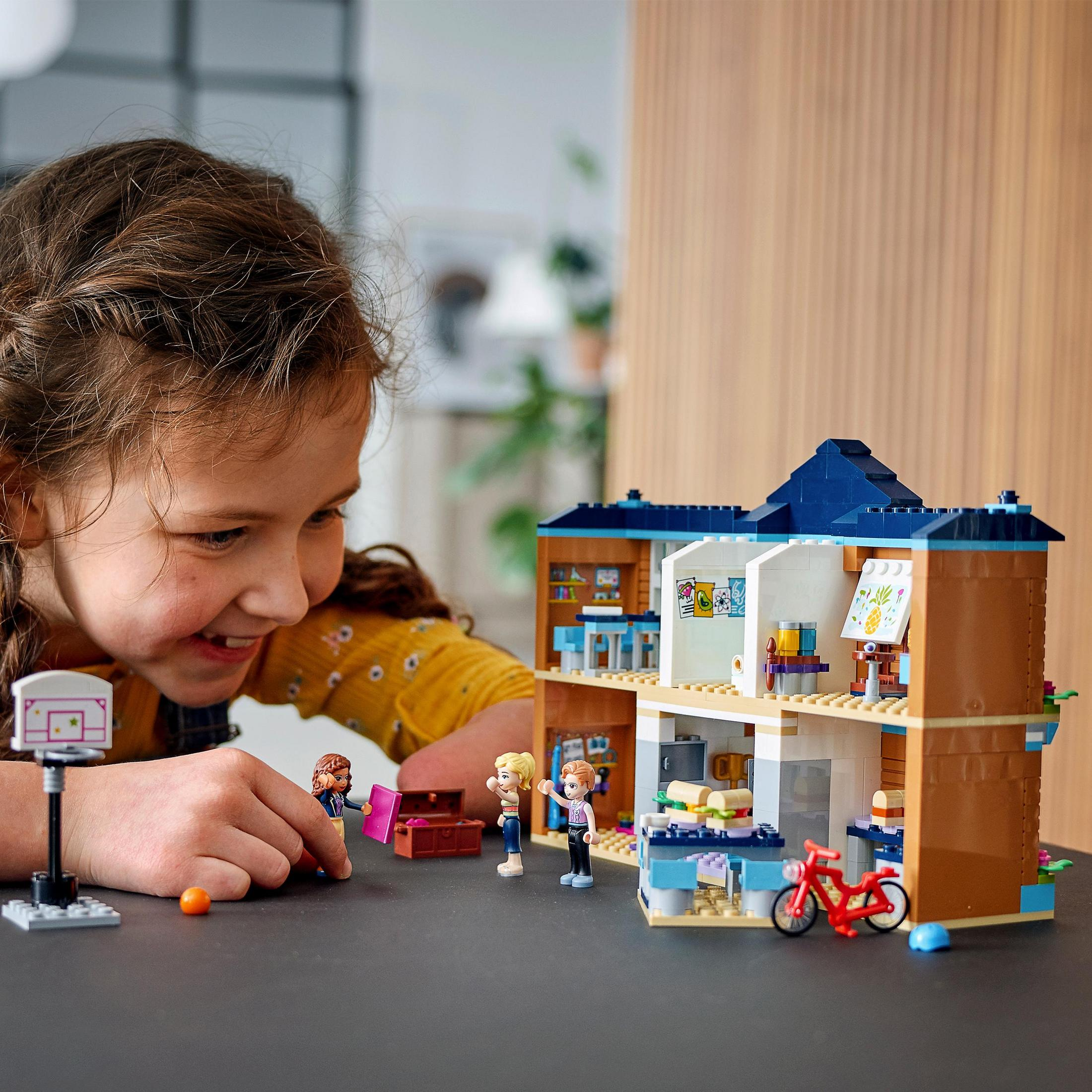 Junges Mädchen spielt mit einem Lego Friends Haus-Set, mit Lego-Figuren und Zubehör.