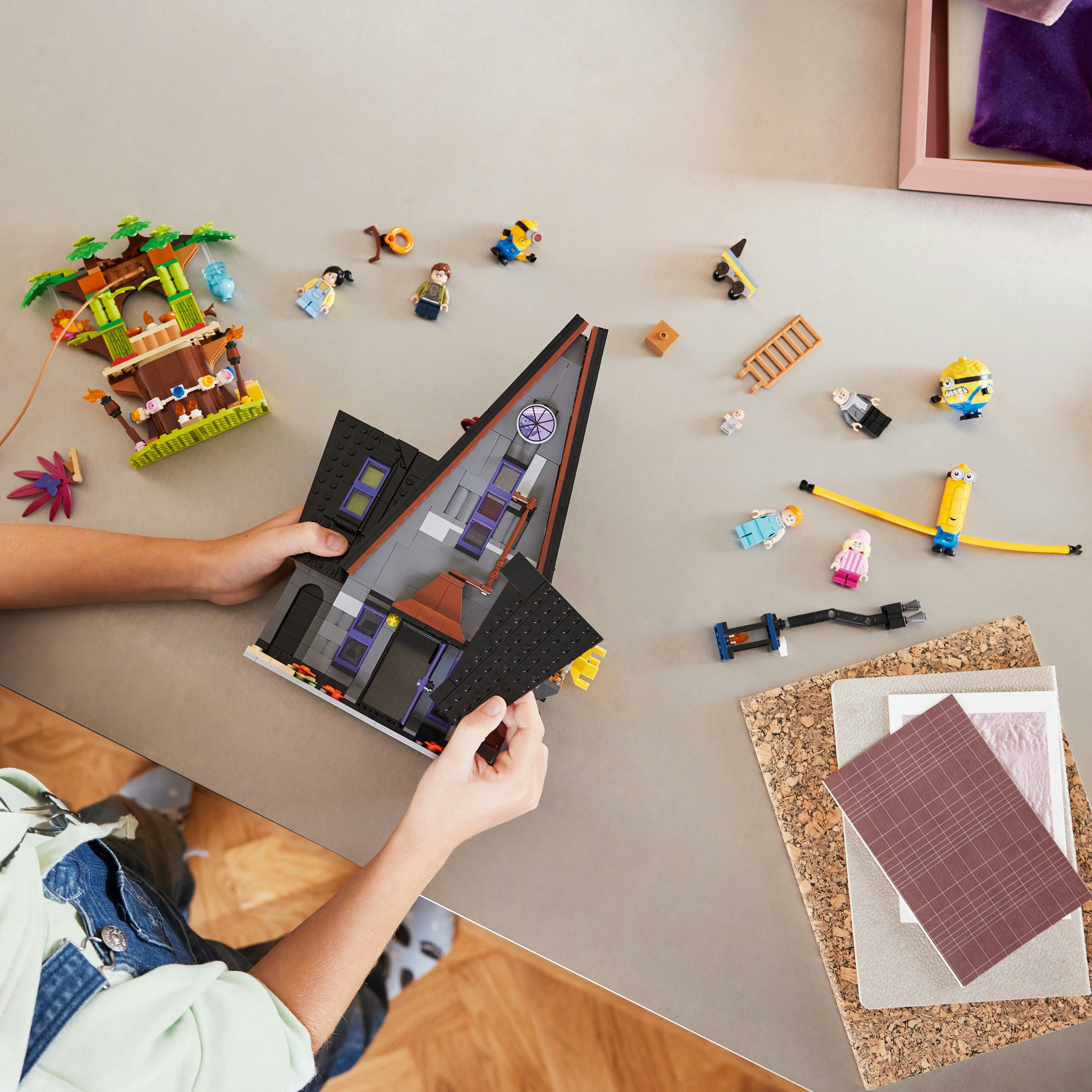 Mains assemblant un set de maison Lego. Autres pièces et figurines Lego éparpillées.