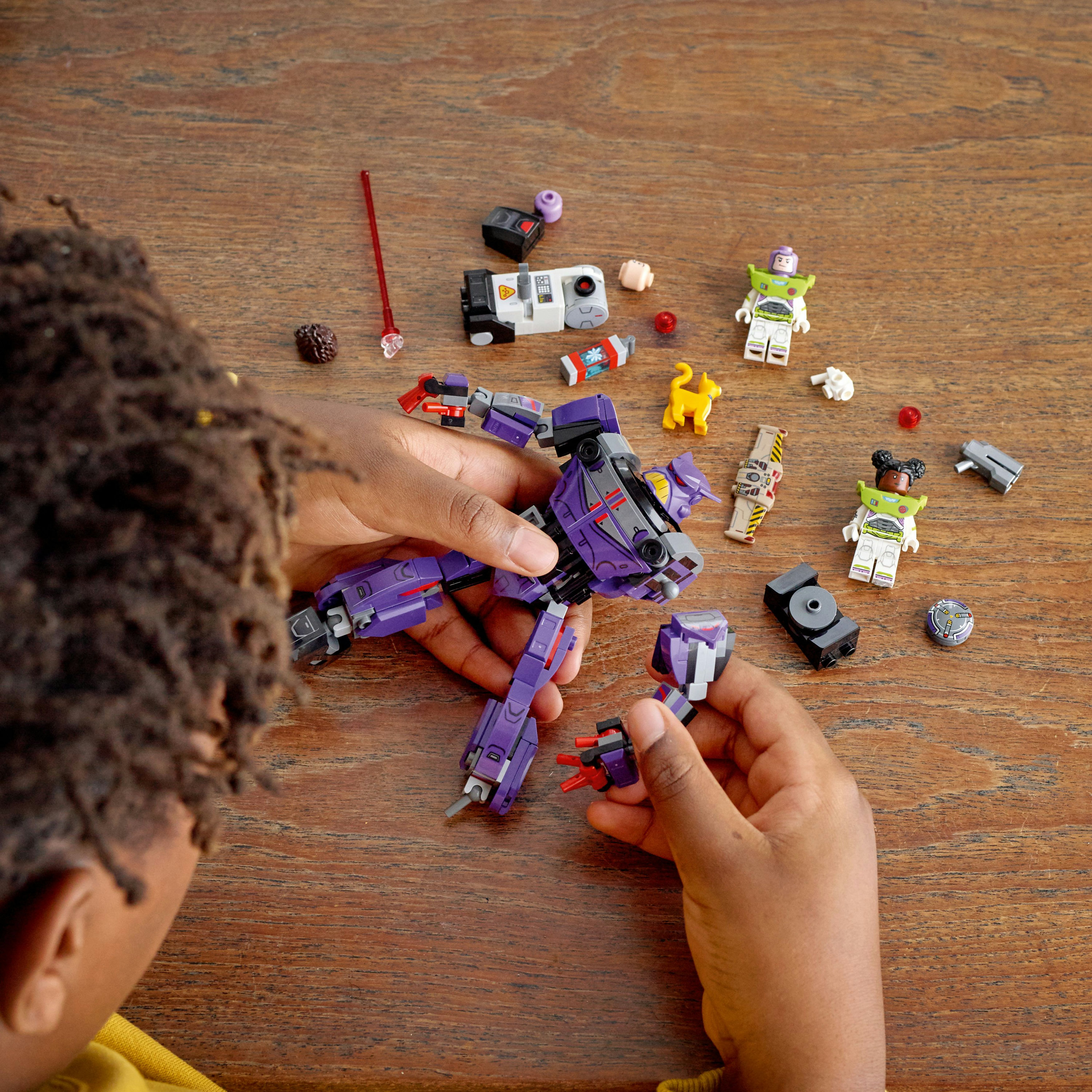 Kind baut lila Buzz Lightyear Lego zusammen. Lego-Teile auf Holztisch verstreut.