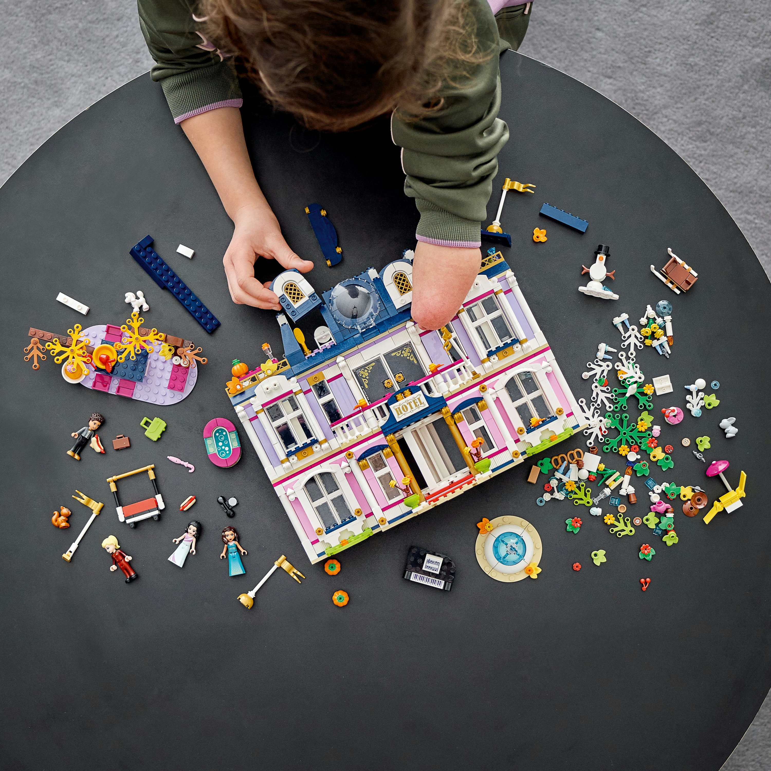 Bambino che gioca con set LEGO Friends su un tavolo nero, assemblando un edificio colorato.