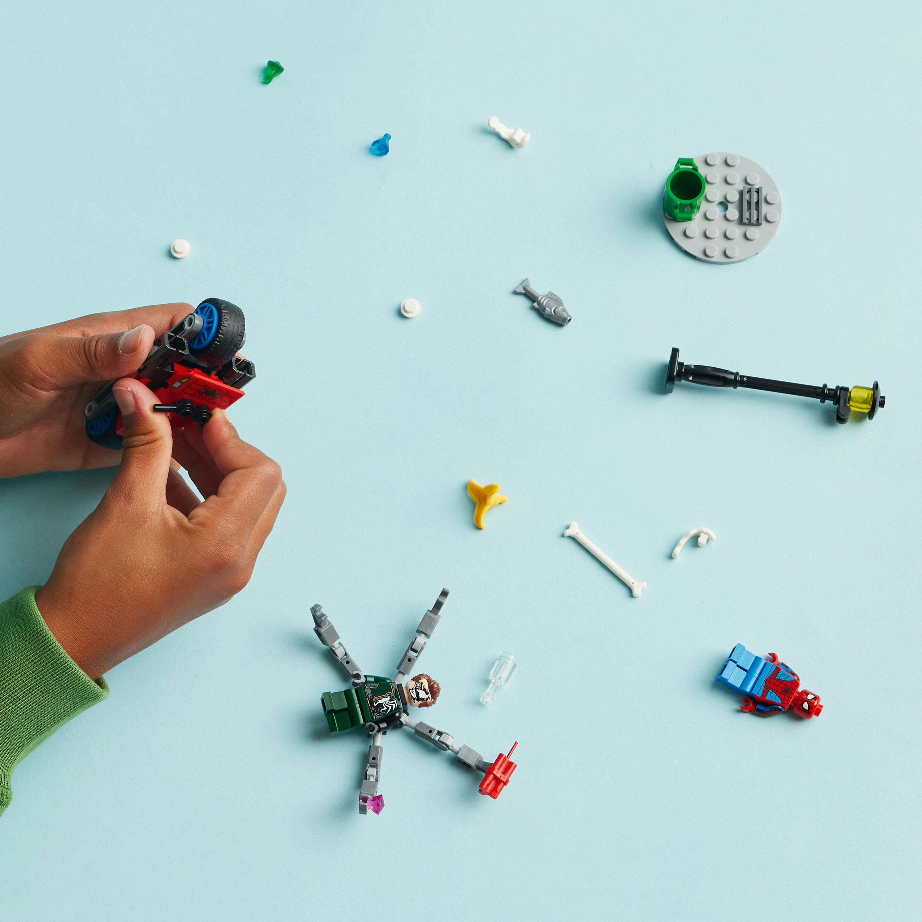 Hände bauen Lego. Verstreute Lego-Teile auf blauem Untergrund. Enthält ein Motorrad und eine Spinnenfigur.