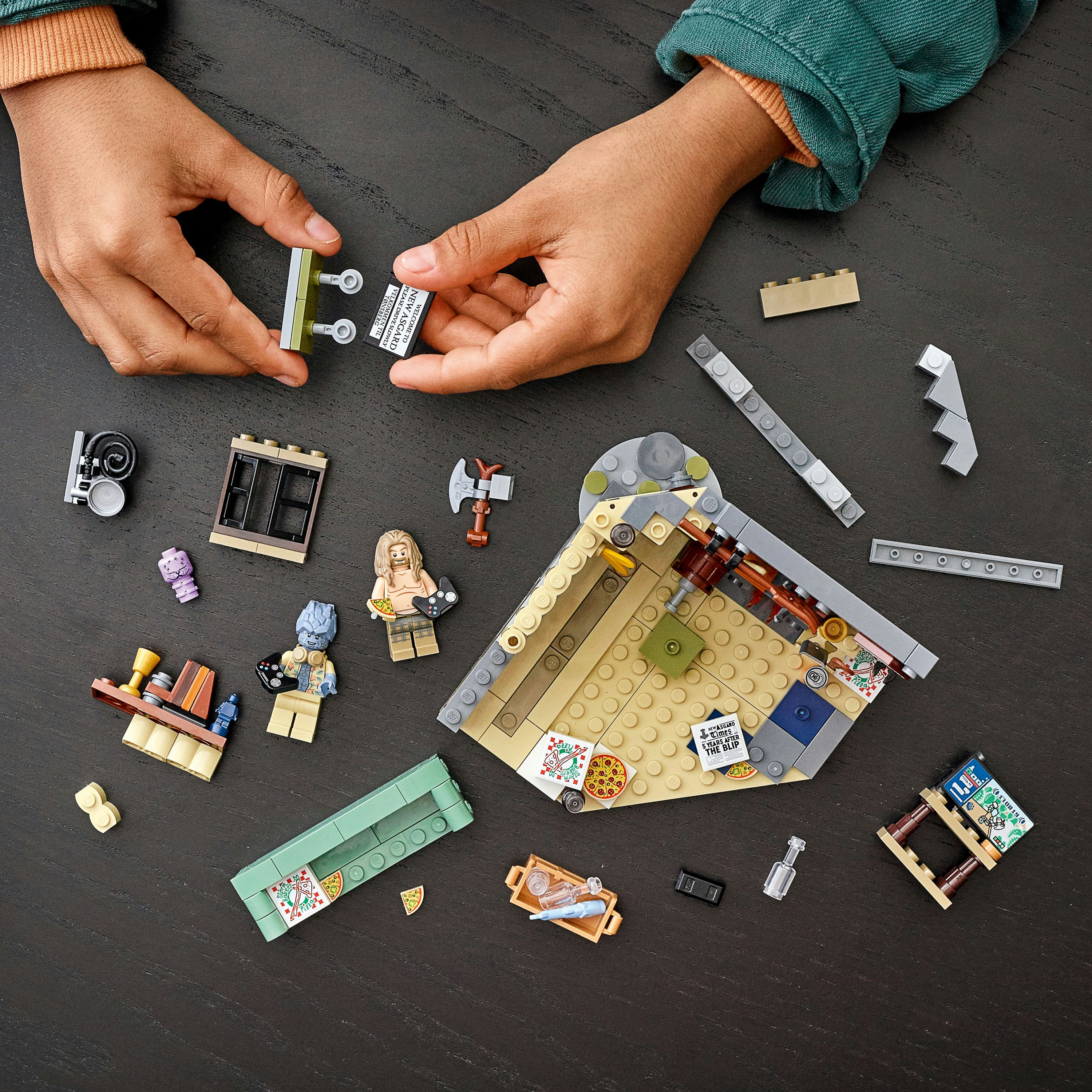 Hände, die LEGO-Set-Elemente zusammenbauen. Verschiedene LEGO-Teile liegen auf dunkler Oberfläche.