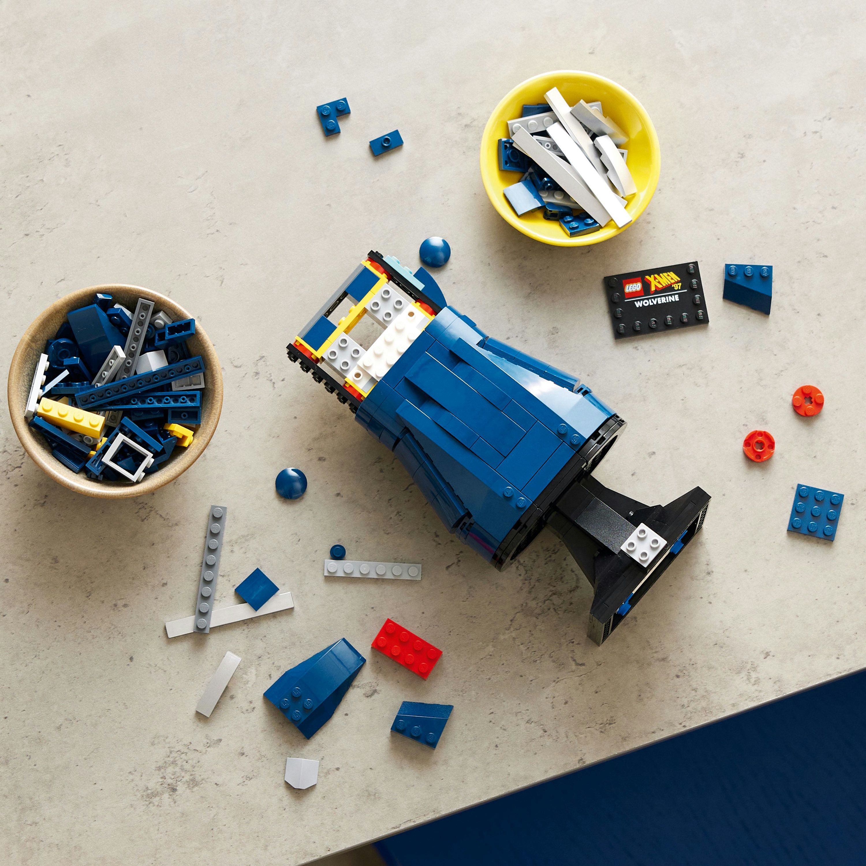 Lego pieces scattered around a blue Lego vehicle, some in bowls, on a gray surface.