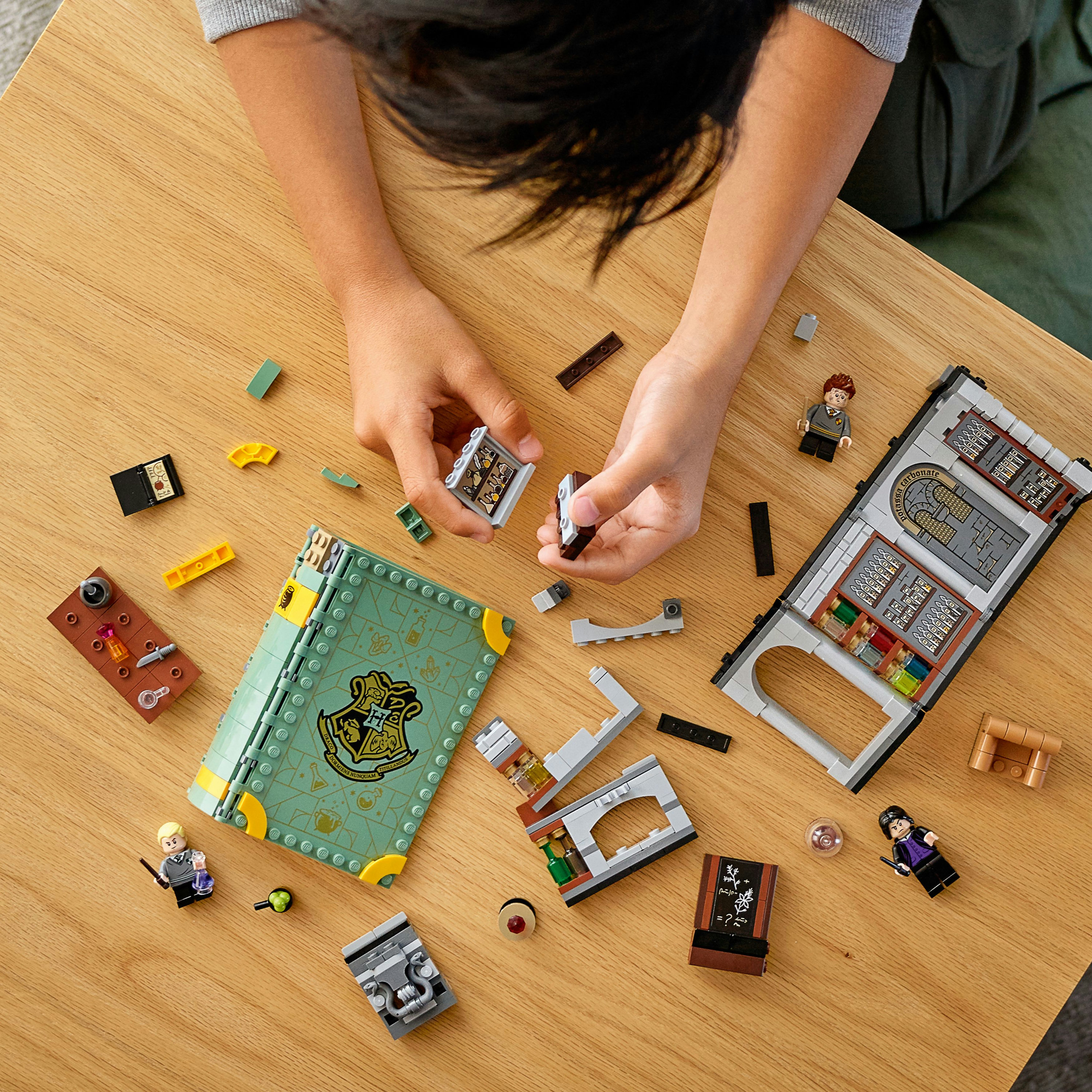 Un niño construye un set de Lego, con un libro y minifiguras sobre una mesa de madera. Vista superior.