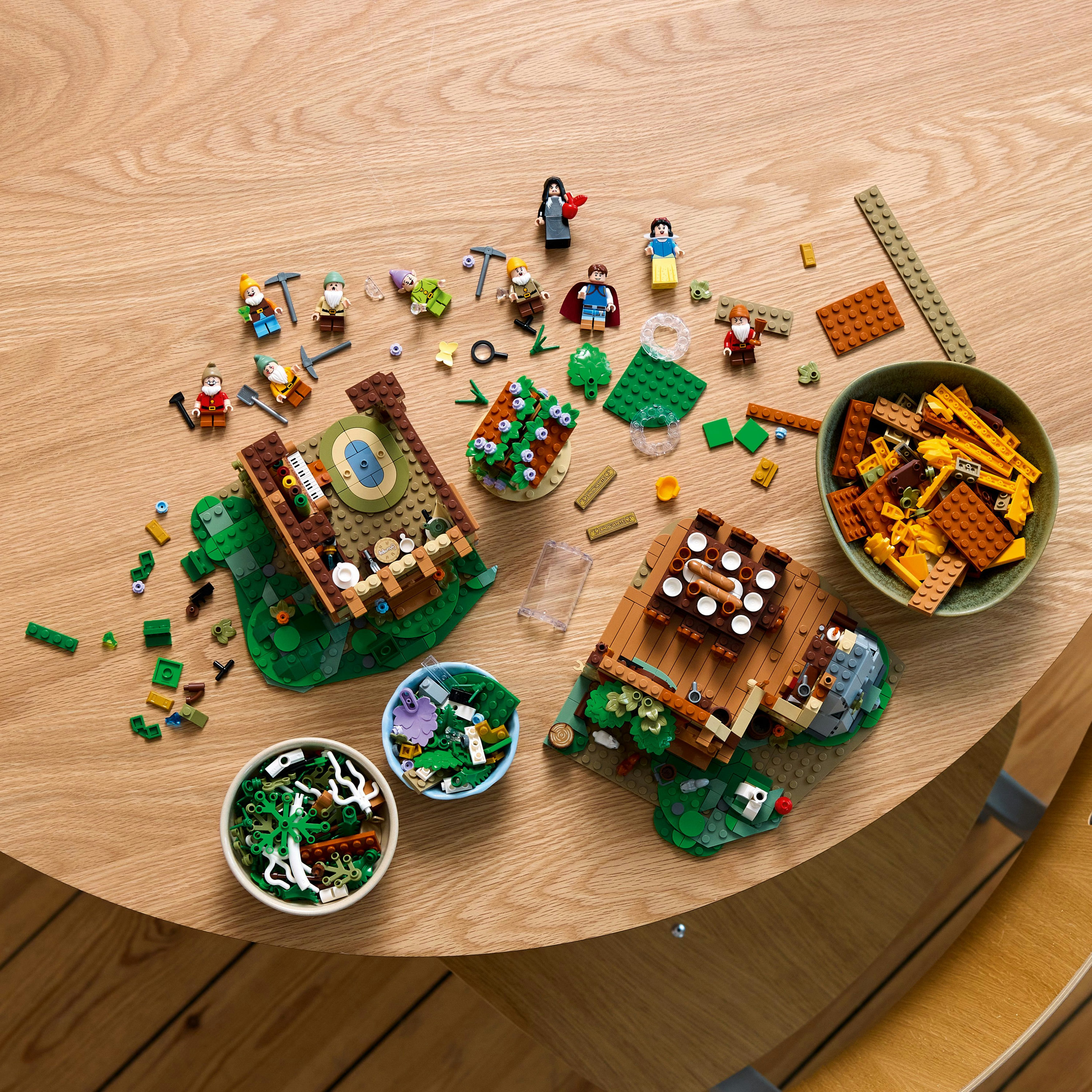 Ensemble Lego avec des figurines, des arbres et des maisons sur une table en bois. Pièces visibles.