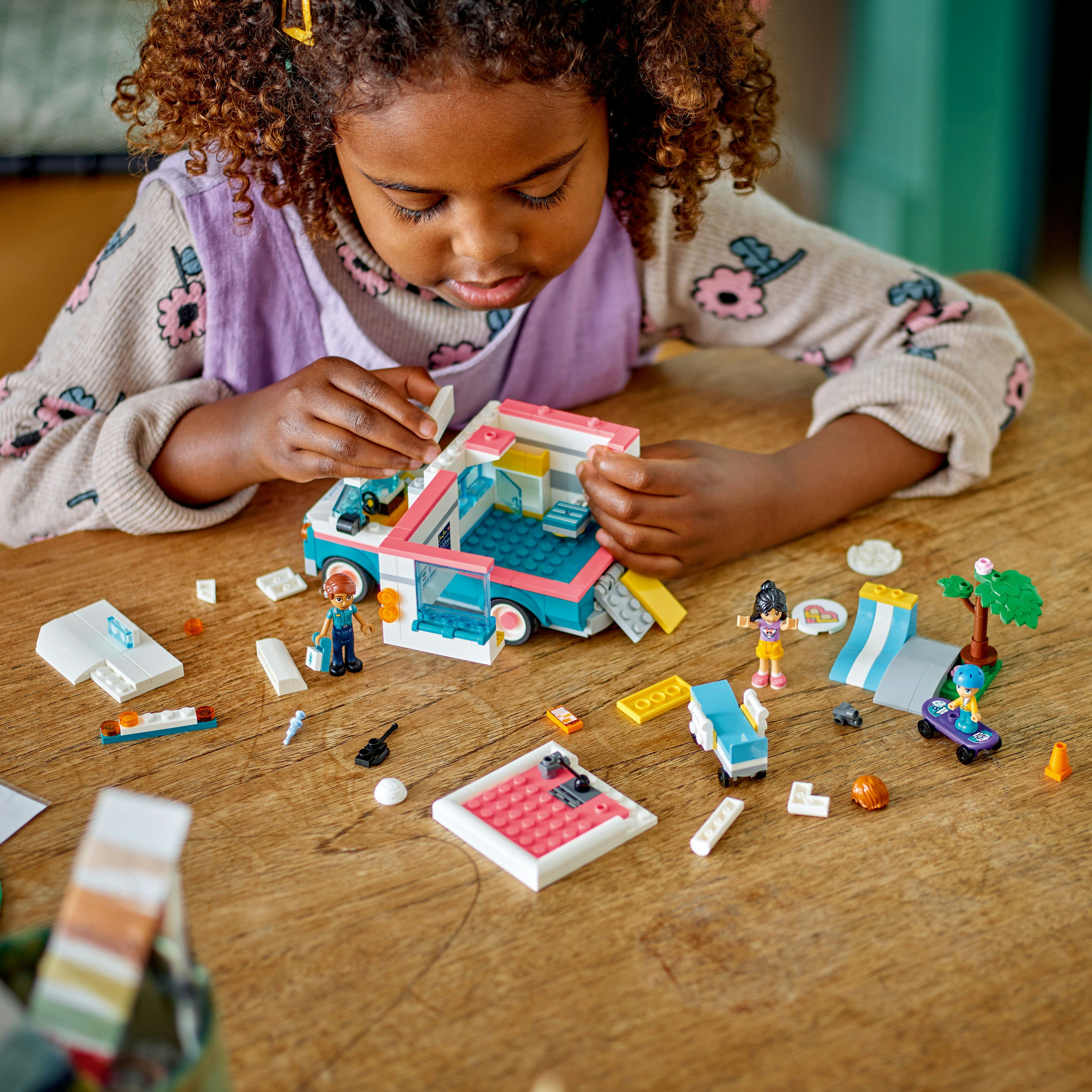 Ahşap masada LEGO Friends setiyle oynayan kız çocuğu.