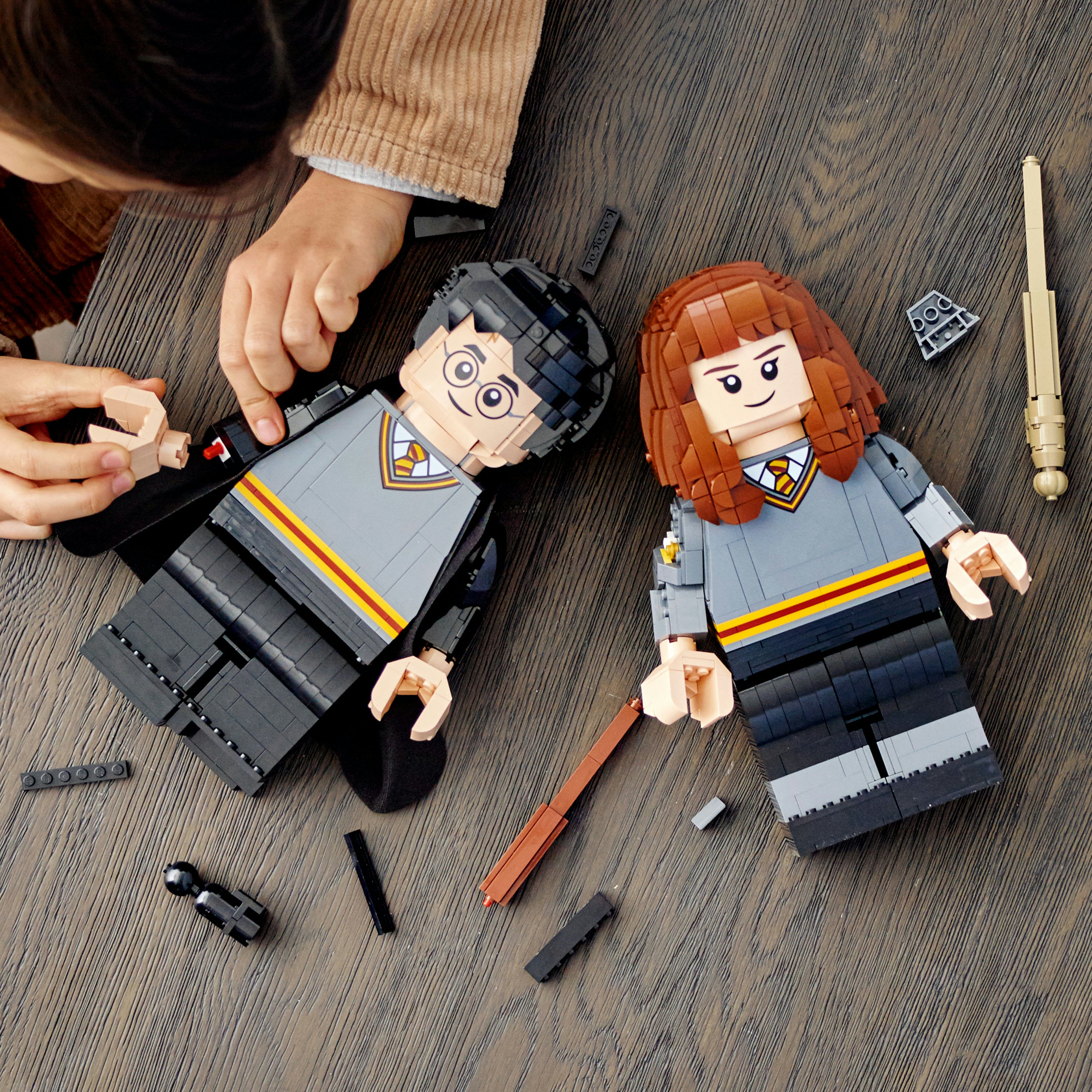 Dwie figurki Lego Harry Pottera i dłonie dziecka na drewnianym stole, z luźnymi klockami Lego.