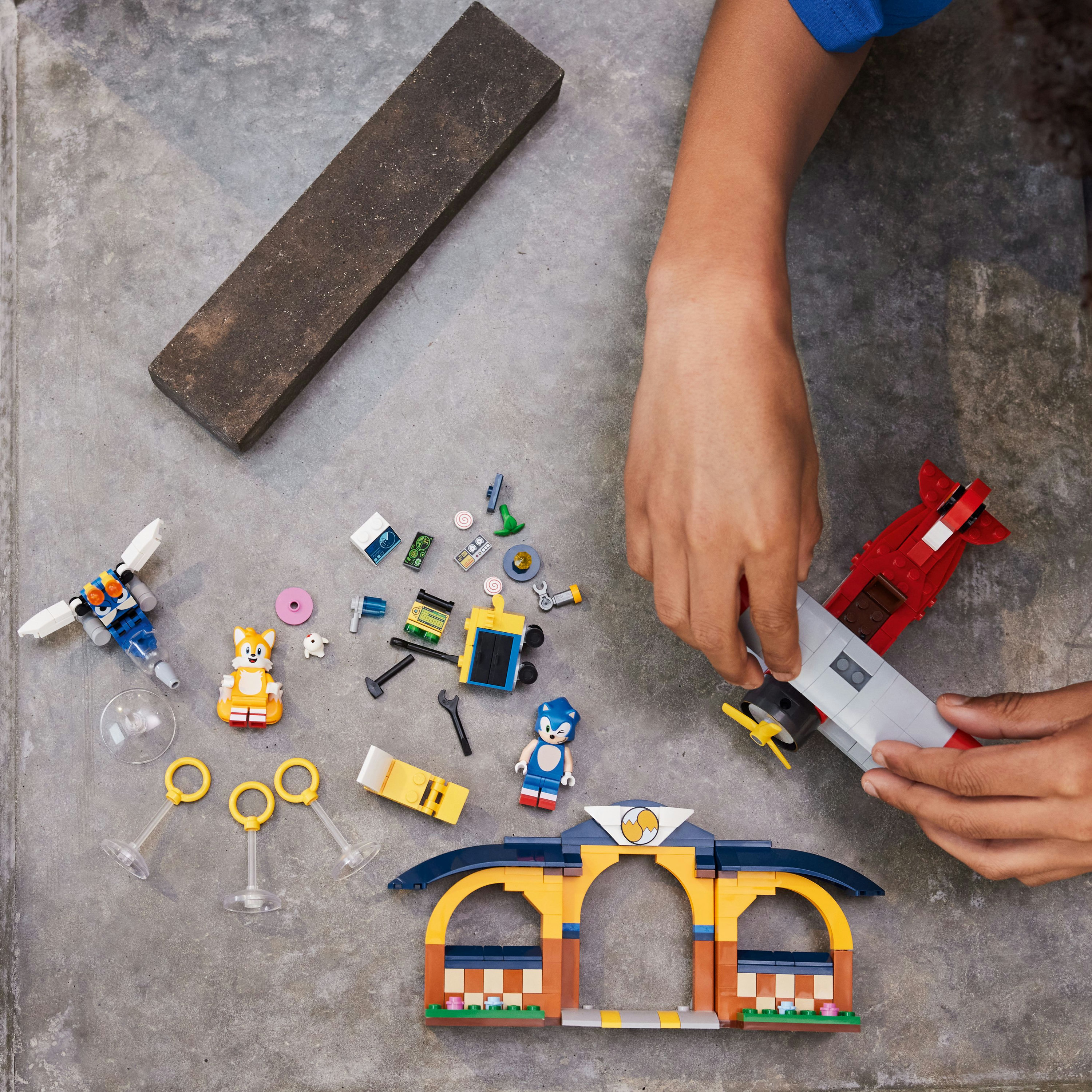 Hände montieren ein Sonic Lego-Set mit Figuren, einem Gebäude und einem rot-grauen Flugzeug.