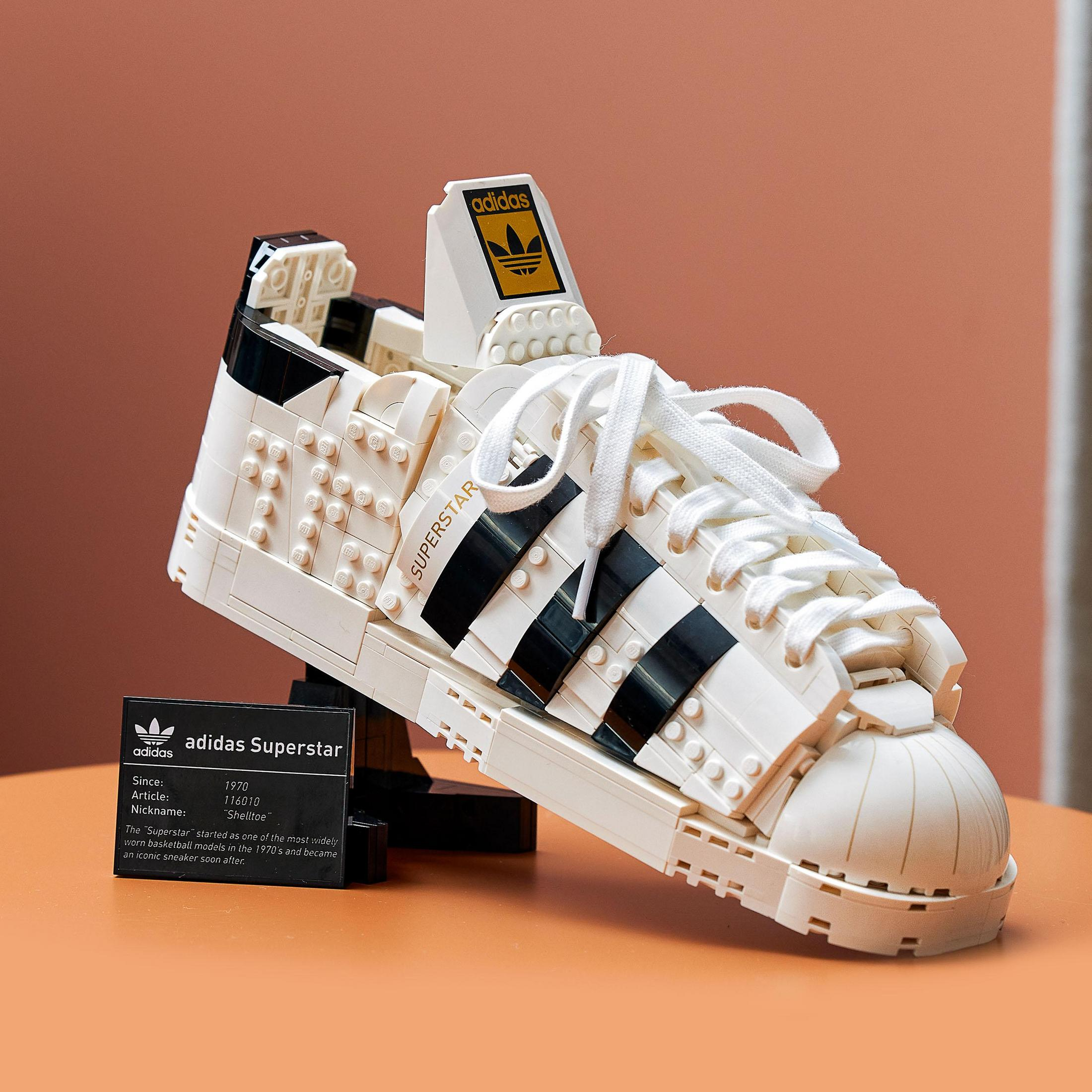 Model buta LEGO Adidas Superstar ze szczegółami, czarnymi paskami i kartą informacyjną.
