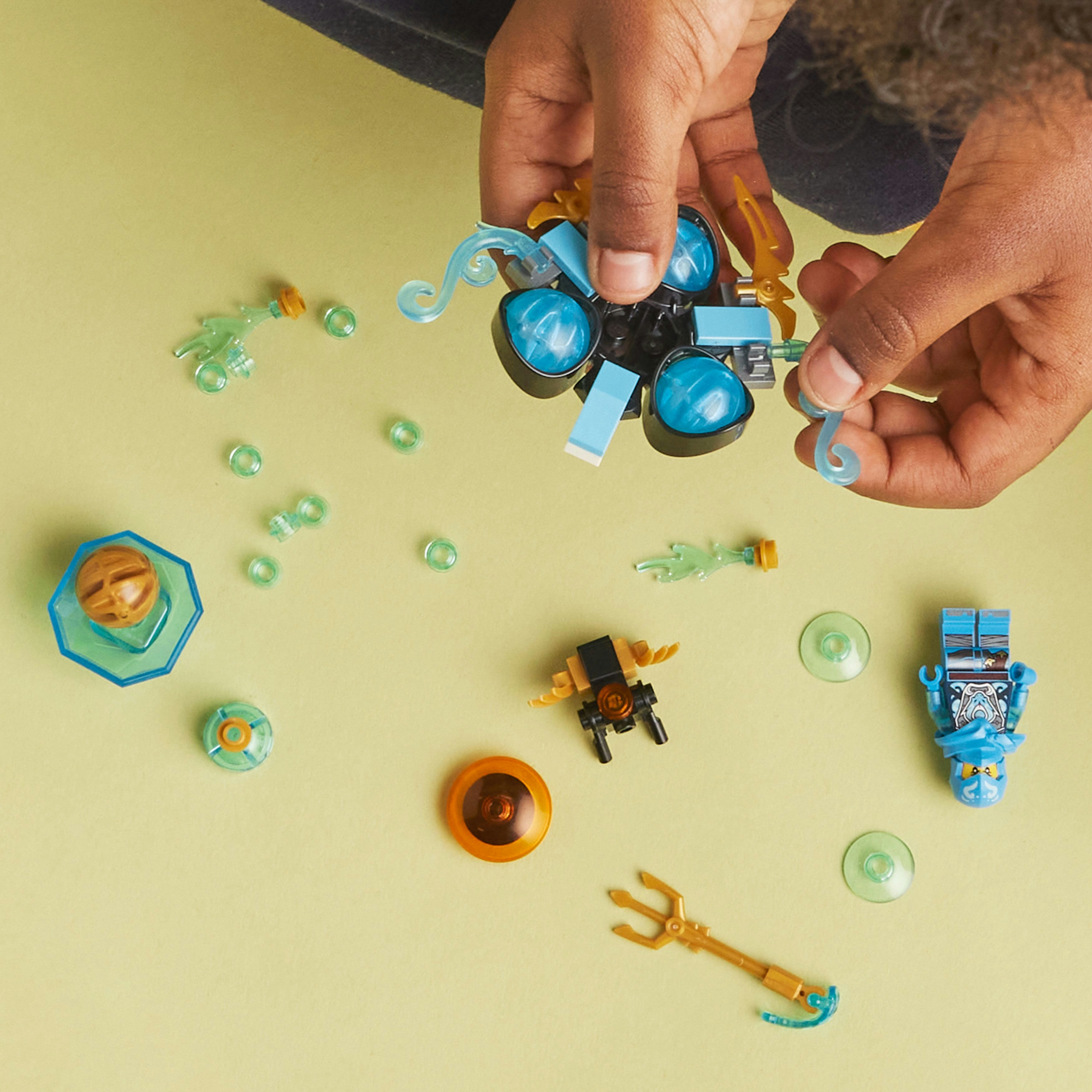 Lego-Teile, Hände bauen ein Spielzeug auf grüner Oberfläche.