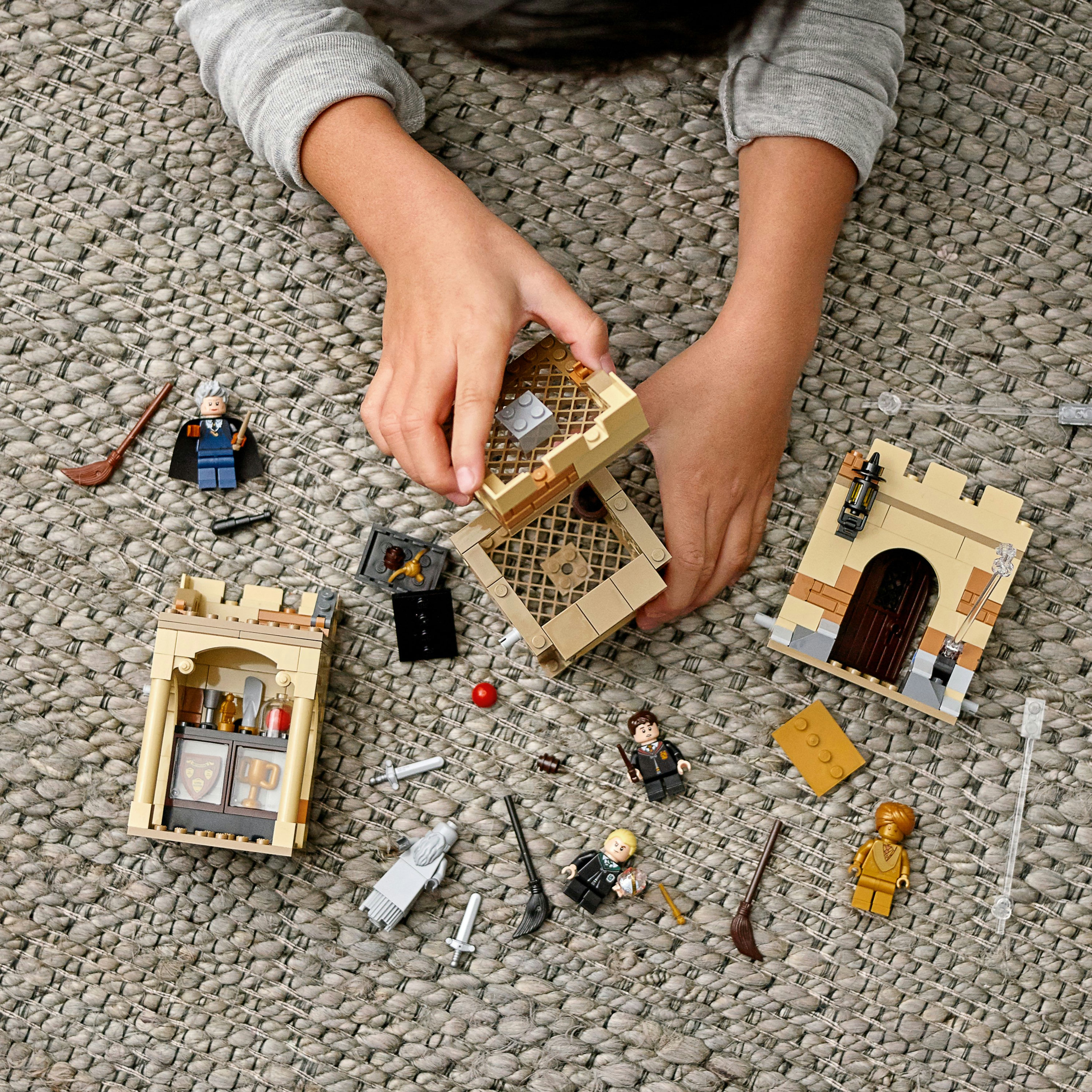 Ręce dziecka bawiącego się różnymi klockami Lego Harry Potter. Szare tło dywanowe.