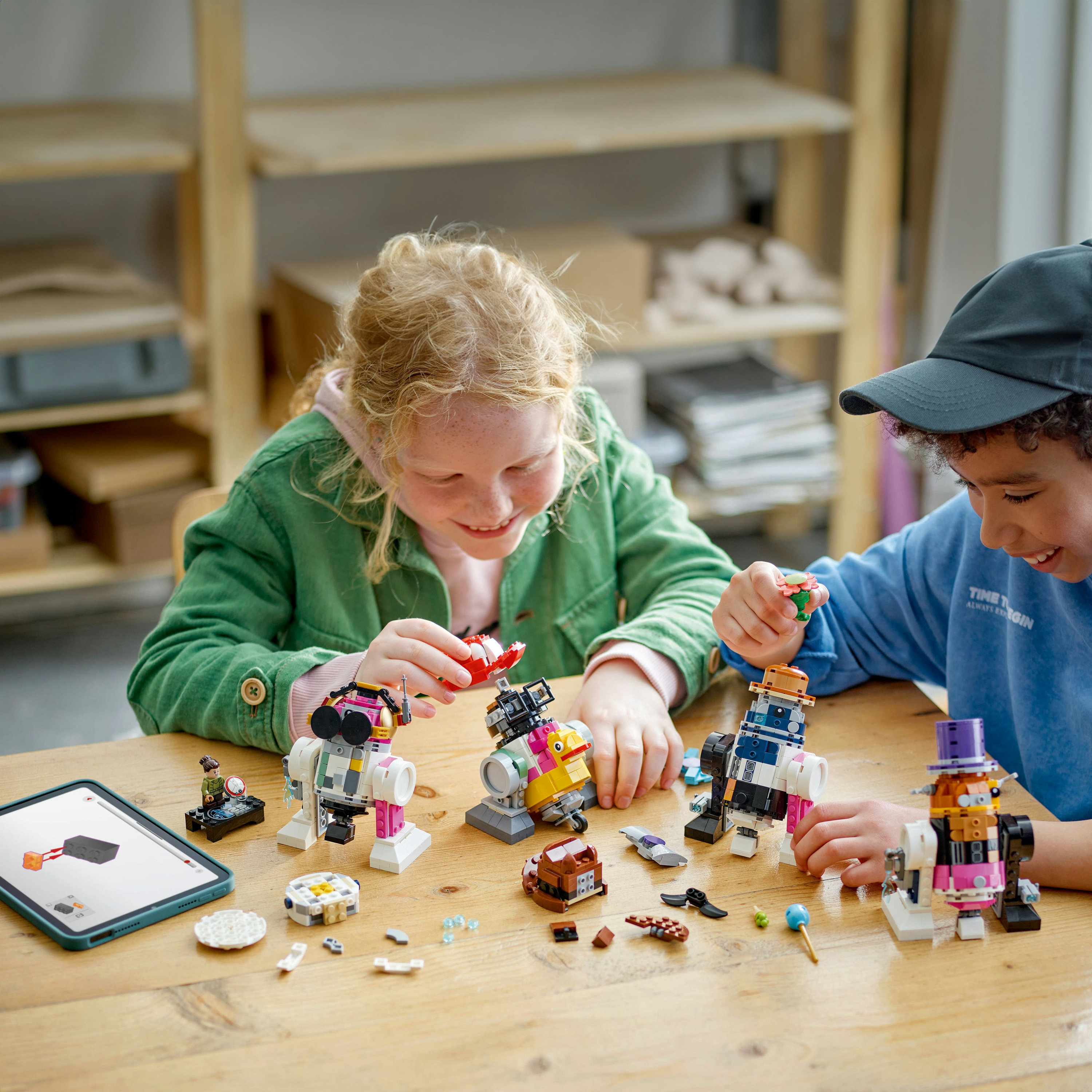 Dzieci budują roboty LEGO na drewnianym stole z tabletem i klockami.