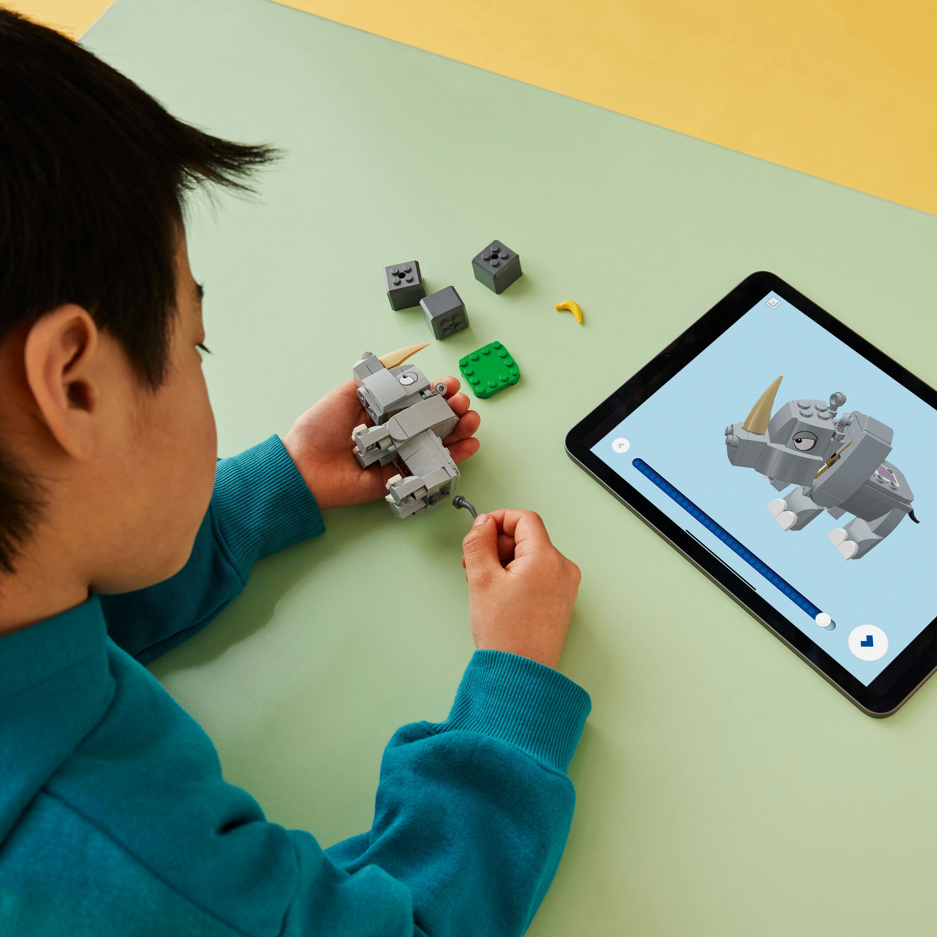 Un bambino che costruisce un rinoceronte Lego con un tablet che mostra le istruzioni.