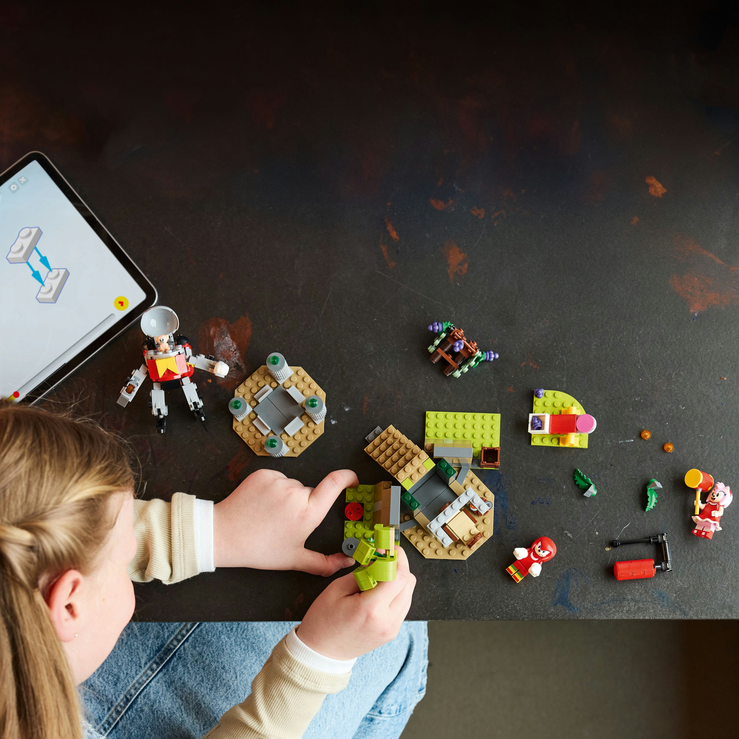 Un niño ensambla ladrillos de Lego. Una tableta muestra instrucciones. Varias piezas de Lego están dispersas.