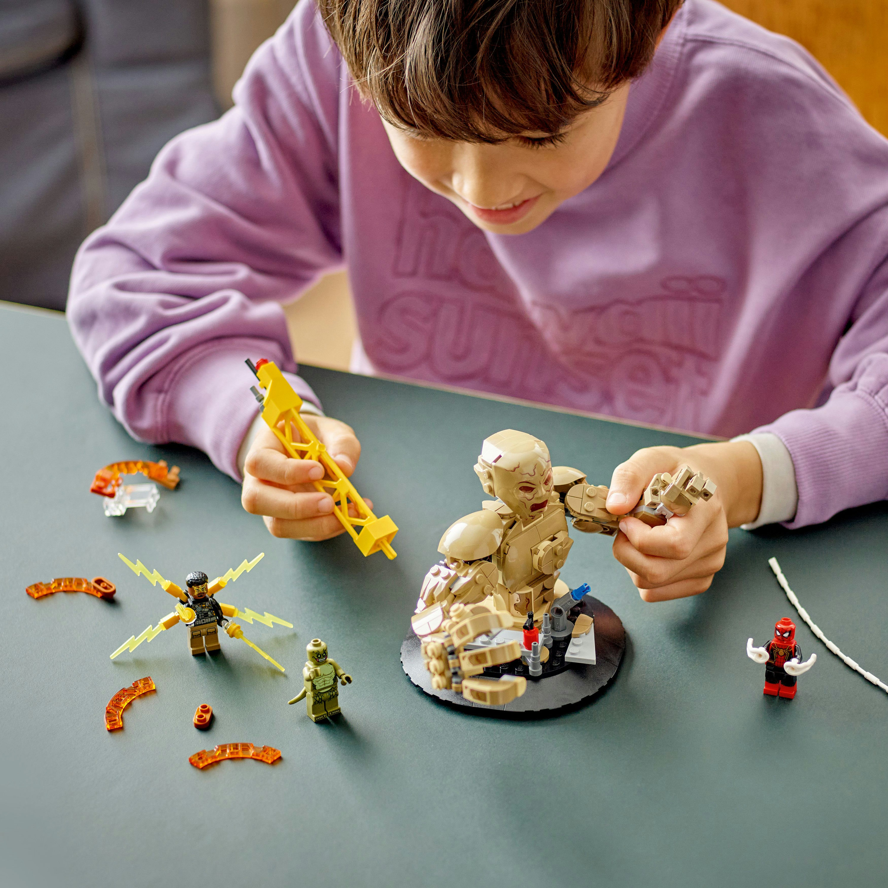 Junge spielt mit Lego Marvel Figuren und Zubehör auf einem dunkelgrünen Tisch, mit einem Spiderman.