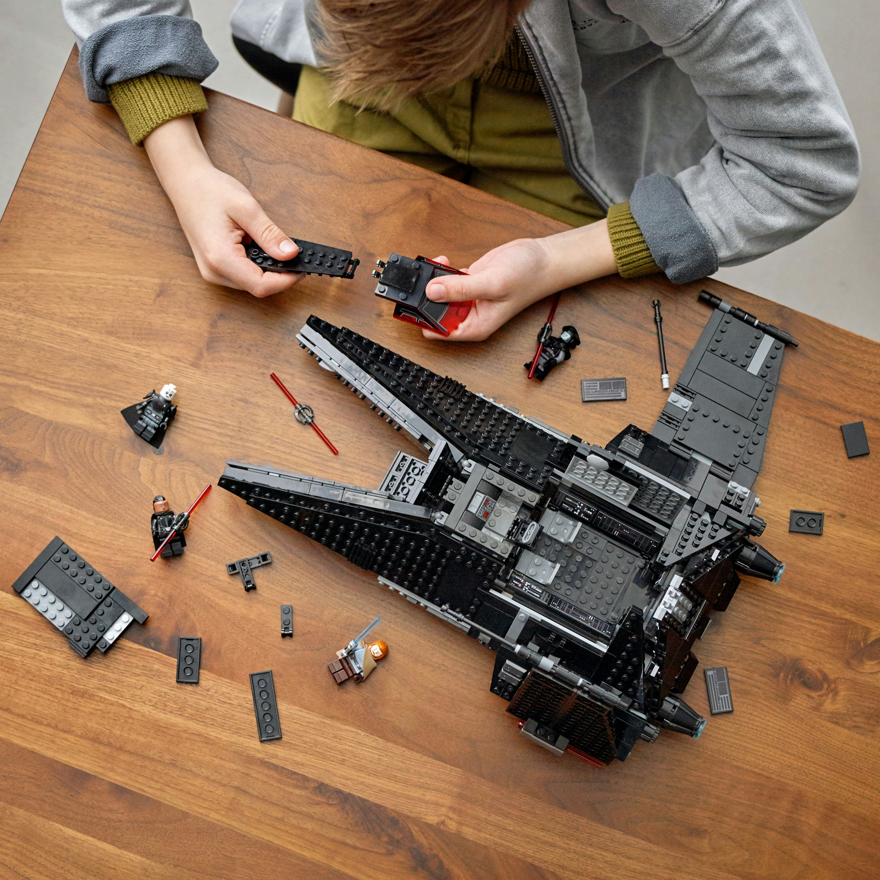 Un niño ensambla una nave Lego Star Wars negra. Hay minifiguras y piezas de Lego esparcidas.